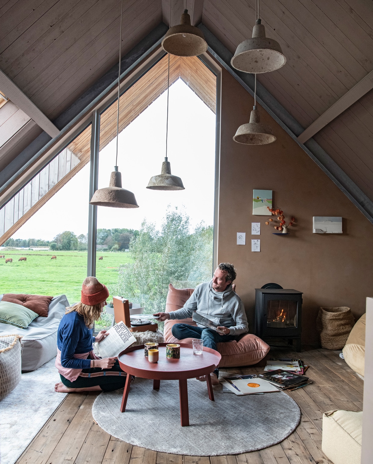 Blauwe en beige zitzakken en harige poef Vetsak. Kussens Wehkamp. Roze stoel Bestwelhip. Salontafel Muuto. Glas Ikea. Kaarsenhouder Sissy-Boy. Hanglampen van Ania Werner. Houtkachel Dru. Mand Fonq. Wandplank Studio de Winkel. Schilderijen met huisjes van Donna Walker via Etsy. Kleden RugVista. Op de muur kalkverf in de kleur Topaze van Pure &amp; Original. vtwonen 11-2021 | styling Esther Jostmeijer | productie Insidehomepage | fotografie Louis Lemaire tekst Inge van Lieshout | tekstbewerking Sunna Borghuis