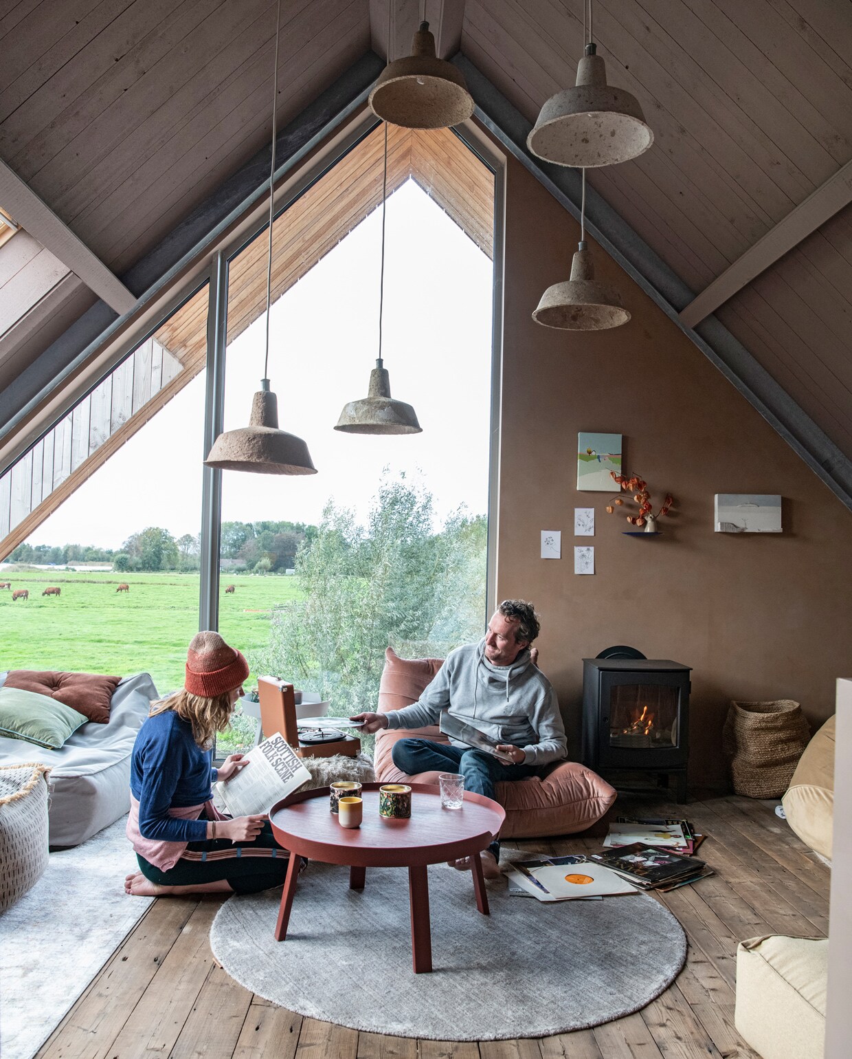 Blauwe en beige zitzakken en harige poef Vetsak. Kussens Wehkamp. Roze stoel Bestwelhip. Salontafel Muuto. Glas Ikea. Kaarsenhouder Sissy-Boy. Hanglampen van Ania Werner. Houtkachel Dru. Mand Fonq. Wandplank Studio de Winkel. Schilderijen met huisjes van Donna Walker via Etsy. Kleden RugVista. Op de muur kalkverf in de kleur Topaze van Pure &amp; Original. vtwonen 11-2021 | styling Esther Jostmeijer | productie Insidehomepage | fotografie Louis Lemaire tekst Inge van Lieshout | tekstbewerking Sunna Borghuis