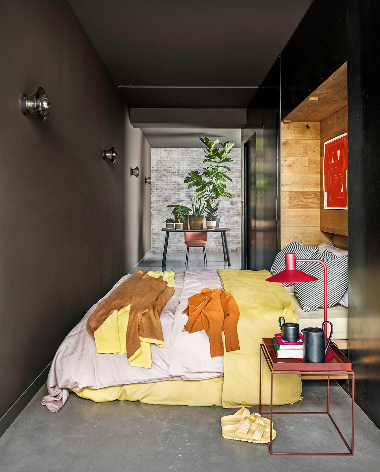 Gele en lila katoen-satijnen dekbedovertrekken Earth van vtwonen, vanaf 200×200/220 cm inclusief kussenslopen € 149,95, grijze gestreepte katoen-jersey kussenslopen, onderdeel van dekbed-overtrekset Comfy Stripe van vtwonen, vanaf € 109,95, bijzettafel van Hay € 175,-, rode lamp van Frantzen € 299,-(vtwonen.nl). Gebreide sprei € 99,95 (suite702.nl). Tafel van Hay € 689,-, stoel van Muuto € 795,-, poster van Hay € 39,- (eijerkamp.nl). Kan en mok met oor van Ferm Living € 55,- en € 19,-(misterdesign.nl). Planten (greenlifestylestore.nl). Vest (scotch-soda.com). Sandalen (birkenstock.co). Overig privébezit. vtwonen 04-2021 | styling Marianne Luning | fotografie Stan Koolen  | assistentie Sasha Landsman, Laura Zuidema | locatie Grace Locations