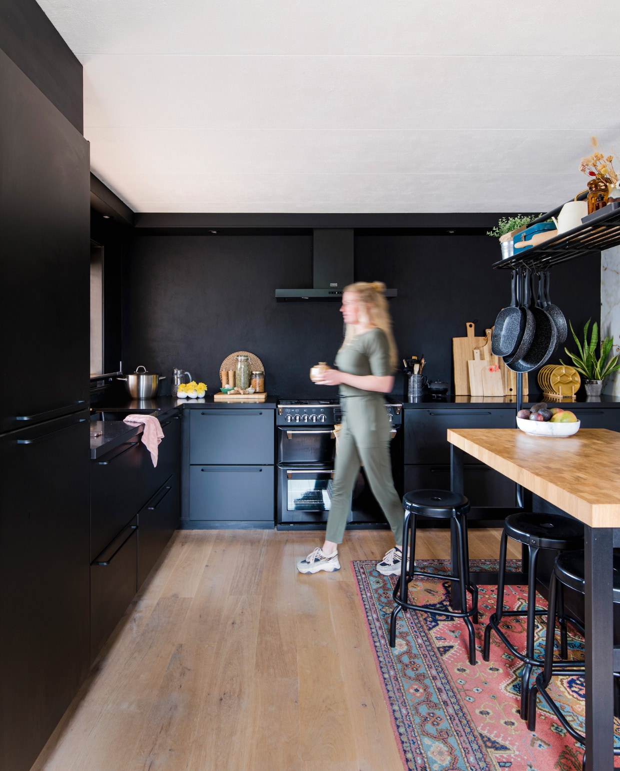 Keuken, hoge tafel en krukken Ikea. Fornuis en afzuigkap Stoves. Karpet en blauwe emaillen beschuittrommel familiestukken. Okergele borden kringloopwinkel. Zwarte theepot Bredemeijer. Snijplanken van Broodt, Xenos, Hema en Ikea. Fruitschaal Bowls and Dishes, hangende pannen Blokker. vtwonen 12-2022 | fotografie Corine Hoge Bavel