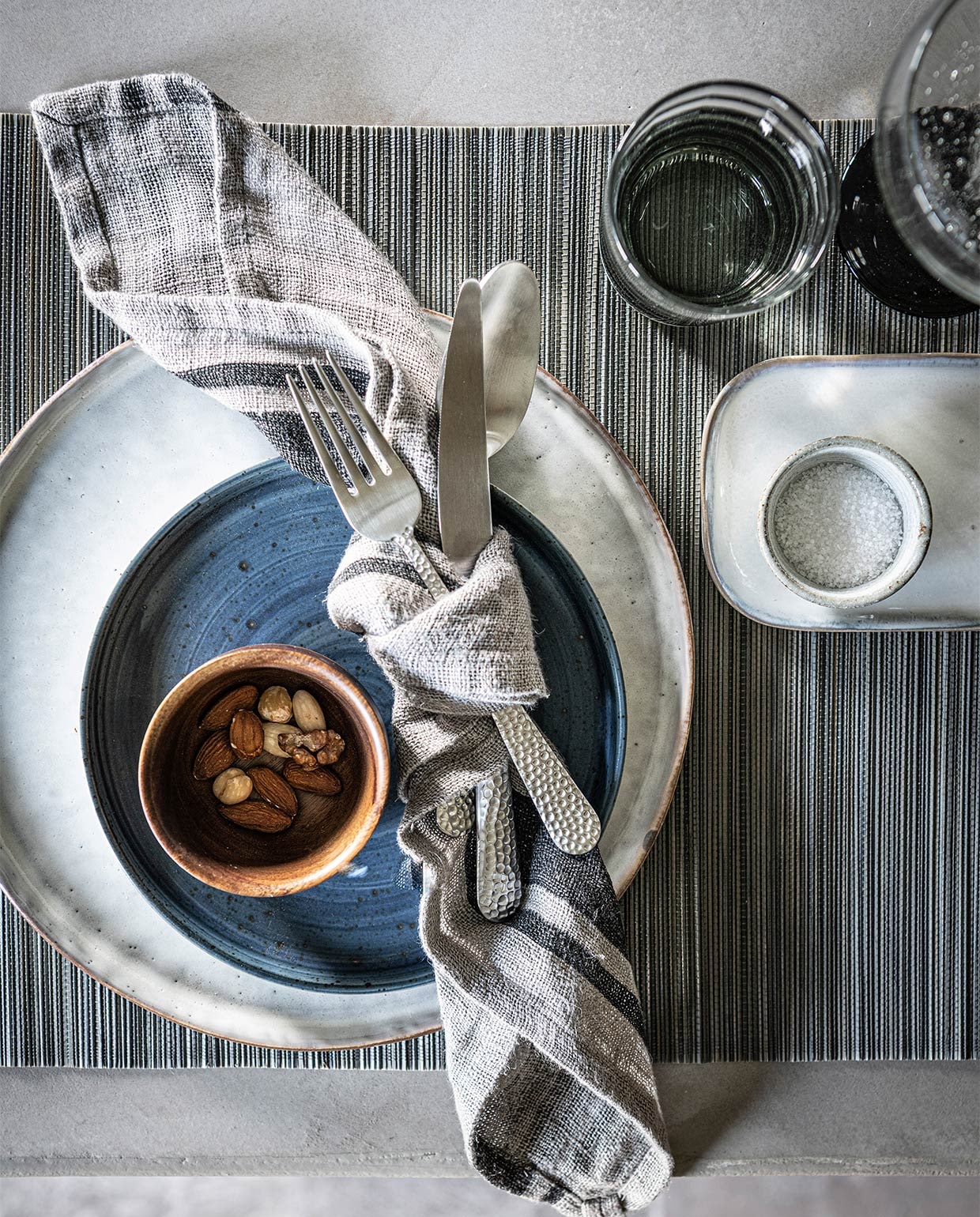 Kom van massief acaciahout van Serax € 13,45 (vtwonen.nl). Gehamerd bestek, per stuk € 5,99, bamboe placemat, set van 2 € 6,99 (zarahome.com). Theedoek van HK Living € 11,95, rond grijs bord van HK Living € 14,95, rechthoekig bord van Serax € 19,95 (loftloft.nl). Blauwe bord € 11,95 (letoile.store). Grijs glaswerk vanaf € 8,95 (nordal.eu). Overig privébezit. JA | vtwonen 11-2021 | styling Kim van Rossenberg | fotografie Sjoerd Eickmans | assistentie Sanne van der Beek en Meike Linthorst
