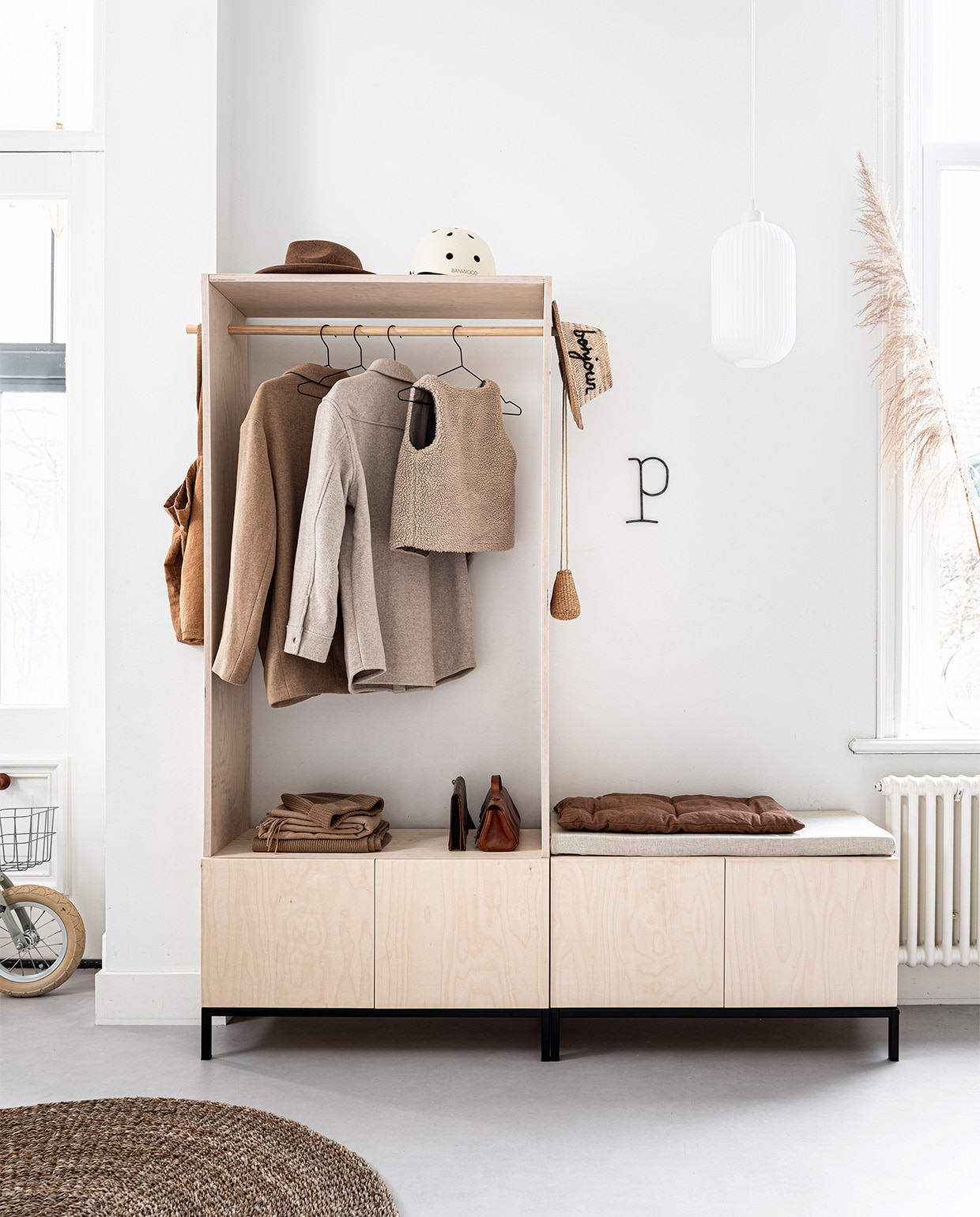 Kast is een DIY. . Zwart onderstel Lowercase, 81x35x12, zwarte kledinghangers van Hay, set van 5, hanglamp Nordlux Milford, 33,5×20 cm (hxØ), vloerkleed van zeegras, Ø 120 cm (vtwonen.nl). Loopfiets (veloretti.nl). Karamelkleurige katoenen tas van Repose Amsterdam (fishonthemoon.com). Bruine wollen hoed (stradivarius.com). Helm cream (banwood.com). Jassen, sjaals en muts, schoenen (stories.com). Kinder bodywarmer (zara.com). IJzeren letter P (stoermetaal.nl). Lichtkussen is zelfgemaakt van schuim, 81×35 cm (abs-schuimplastichuis) met linnen stof (deboerenbonthal.nl). Donkerbruin kussen Futon Aki cushion, 60x34x3-4 cm (woodchuck.nl). Leren tasjes, rieten hoed, rieten tasje, kinderschoenen privébezit. vtwonen 03-2020 | styling Kim van Rossenberg | fotografie Sjoerd Eickmans