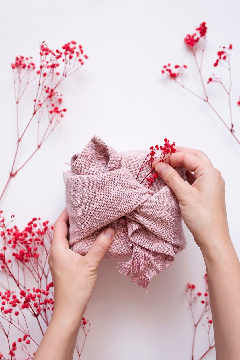 Gift box in natural fabric holds in hands on white background with red dry flowers. Eco and sustainable gift wrapping ideas. Festive backdrop Furoshiki wrap. Recycling and eco-friendly alternatives. Getty Images/iStockphoto