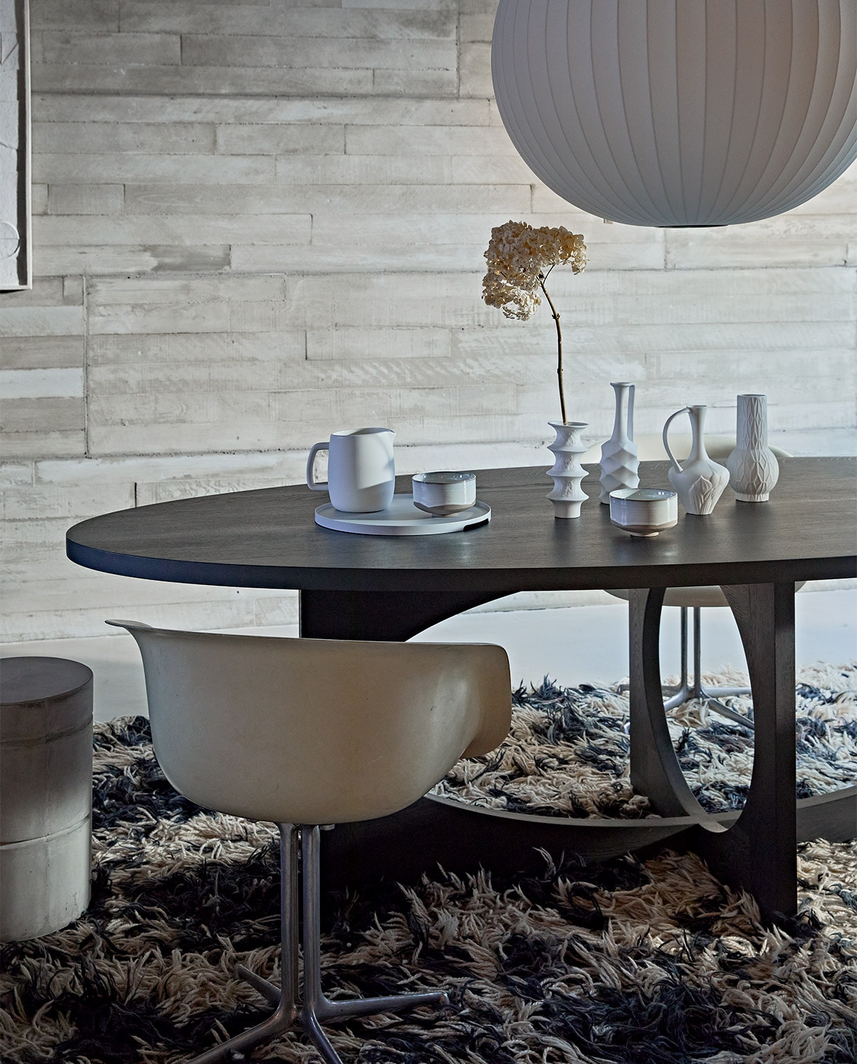 Zwartgebeitste massief eikenhouten ovale tafel van ontwerper Sarah Trenite, 260x115x75 cm (lxbxh), prijs op aanvraag (arpdesign.com). Vintage La Fonda kuipstoel van Eames voor Herman Miller, prijs op aanvraag (pietjonker.nl). Grote witte vazen Cobra Bubble tall € 120,- en Double Bubble tall € 135,- van 101CPH (edha-interieur.nl). Schilderij met reliëf, 100×70 cm € 199,- (urbannatureculture.nl). Kleine vazen van HKliving, set van 4 € 129,95, keramieken waterkan van ontwerper Vincent van Duysen voor Serax, 1,5 liter € 25,-, hanglamp Nelson Ball Bubble van Hay, 68 cm (Ø) € 607,99, dienblad van Zone Denmark, 35 cm (Ø) € 50,-, kommen Merci n°1 van Serax, 12,5 cm (Ø) per stuk € 16,65 (vtwonen.nl). Betonnen kruk van Marie Michielssen, 30×45,5 cm (Øxh) € 103,- (serax.com). Gedroogde hortensia’s (edenique.nl). Soortgelijk vintage vloerkleed (vintagehoarder.com). JA | vtwonen 02-2022 | styling Cleo Scheulderman | fotografie Jeroen van der Spek