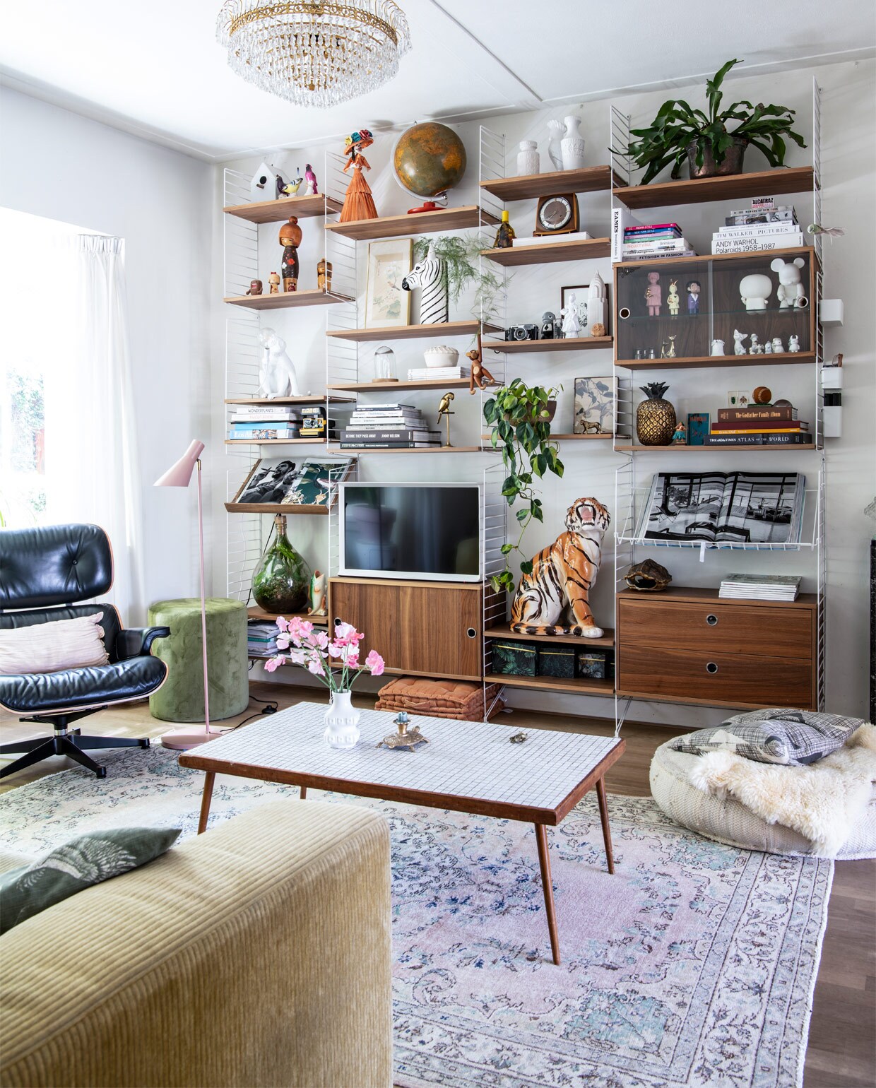 Bank Leolux, kleed Rozenkelim. Eames Lounge Chair en String-kast Co van der Horst. Plafondlamp straatvondst, vloerlamp Kwantum. Groene poef Riverdale, matraskussens Day Home, ecru poef Lodsh. Kussen Livv lifestyle. Tafel en ornament kringloop, kandelaar Sissy-Boy, vaas West Germany. In kast: zebra- en visvaas en lijst met print Sissy-Boy, aap Kay Bojesen, tijger, ornament vogel en klok Dolores del Dia. Tekening Mark van Gennip (mrrk.nl), ananas Zara Home. Overige souvenirs en vintage. vtwonen binnenkijk special 12-2020 | productie Insidehomepage | styling Kim Timmerman | fotografie Louis Lemaire | tekst Inge van Lieshout | tekstbewerking Mariska keus