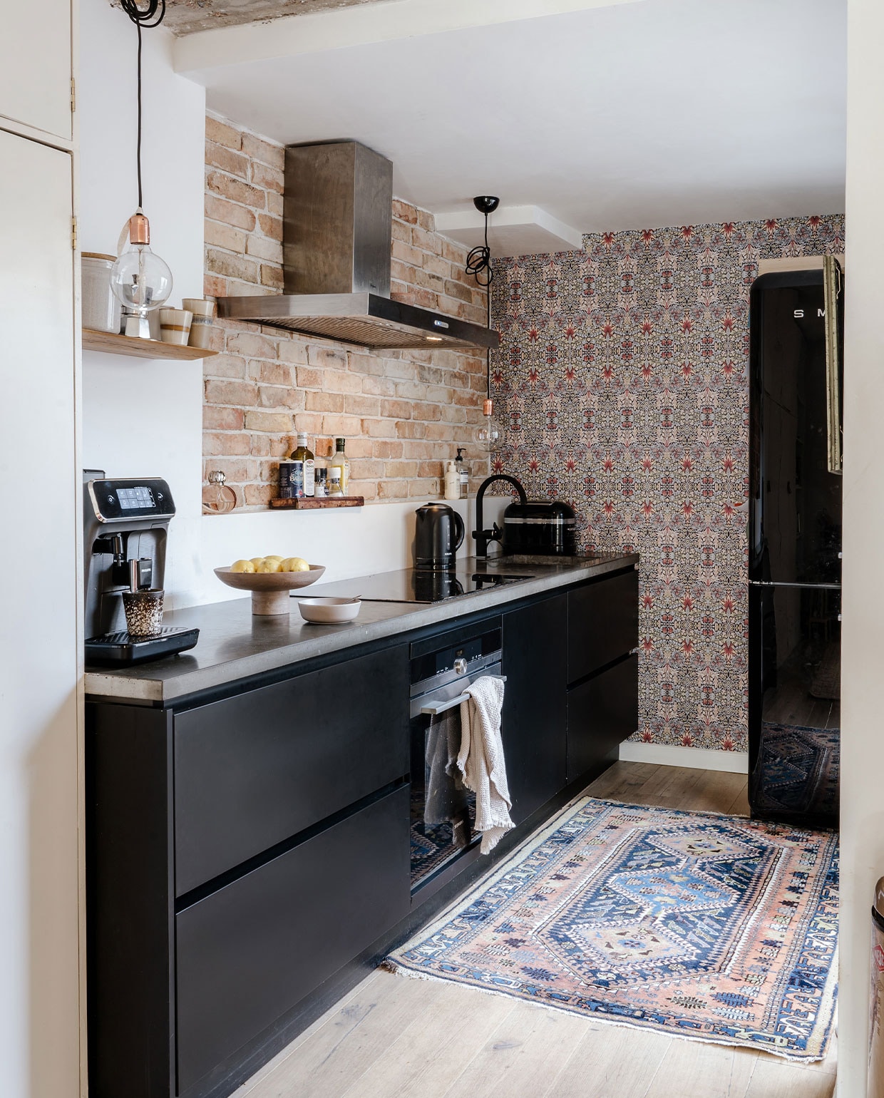 Behang Morris &amp; Co, houten vloer Basic Floors, kleed vintage, keuken Keukenloods, lampen zelfgemaakt, fitting Loods 5, theedoek en fruitschaal H&amp;M Home, koffiezetapparaat Philips, mokken HKliving, broodrooster KitchenAid, waterkoker Krups, koelkast Smeg, schaal By Lille Vilde, koekblik Hema, houten plank Sissy-Boy. NEE | vtwonen 6-2022 | productie CocoFeatures | styling Laurien Deken | Fotografie Inge Korver | tekst Robin Pakvis