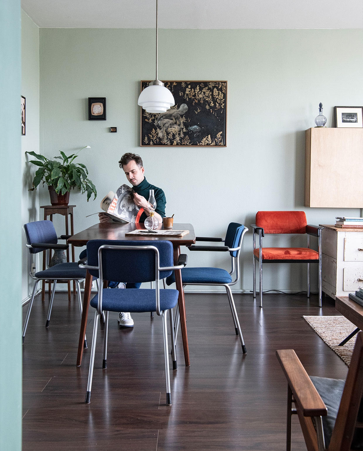Vloer Ikea, muurverf Mizzle van Farrow &amp; Ball. Eettafel en oranje stoel cadeau gekregen, eettafelstoelen en hanglamp Gispen. Planttafel Marktplaats, vloerkleed Zara Home, televisiekast zelfgemaakt, fauteuil Rob Parry via Marktplaats. Kunst van links naar rechts Daniela Schwabe, Maze de Boer, Luis Xertu. Overig onbekend. NEE | vtwonen 6-2022 productie Insidehomepage | styling Kim Timmerman | fotografie Louis Lemaire  | tekst Anne-Flore Muller