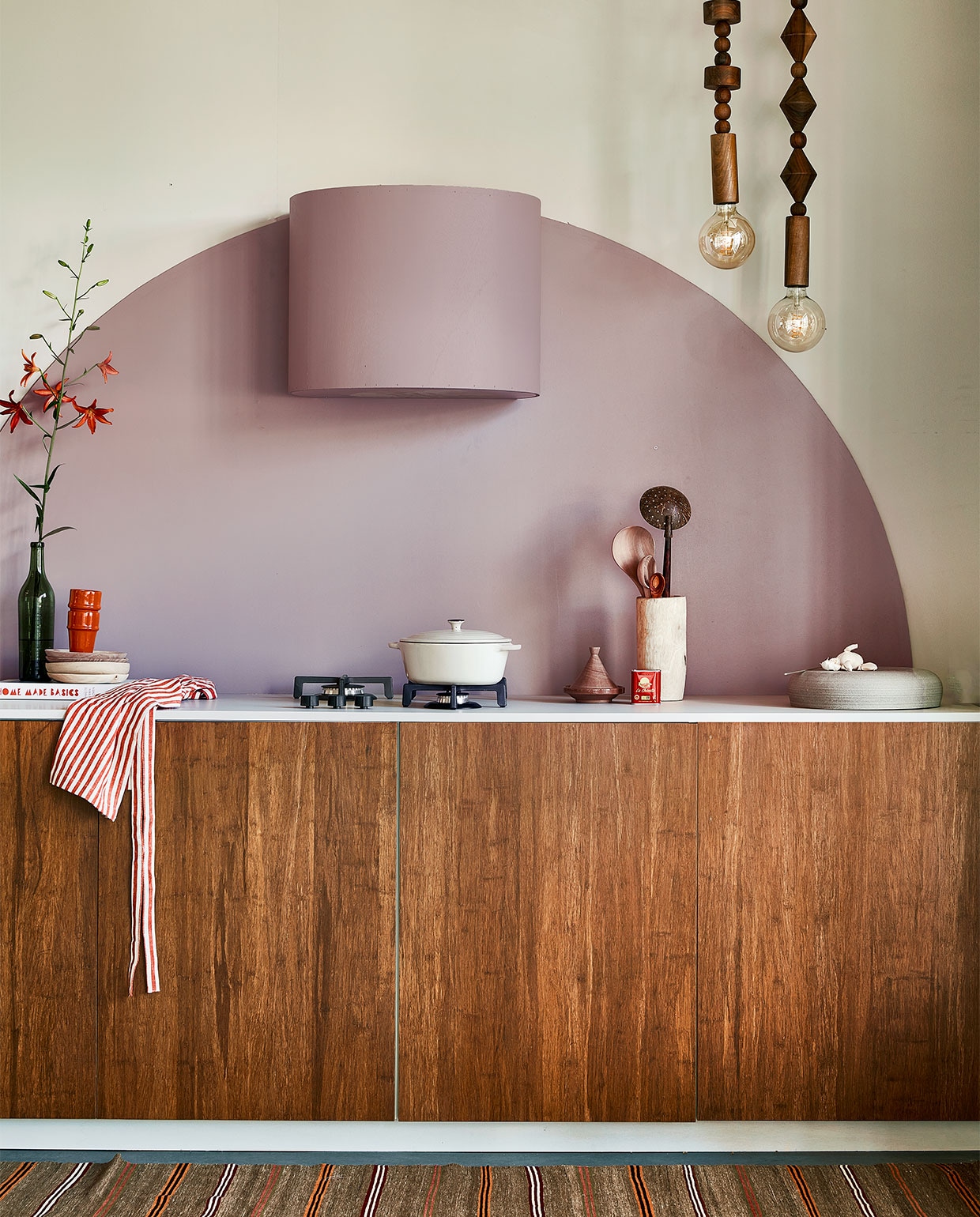Muurverf Flexa Easycare Keuken kleur Cosmic Glory, ronde vorm en bekleding afzuigkap kleur Heart Wood, per liter € 25,49 (flexa.nl). Bamboe fronten Destiny Caramel, 60×80 cm (bxh) € 259,-, aanrechtblad prijs op aanvraag (frontz.nl). Vloerkleed vintage, 215×86 cm € 350,- (rozenkelim.nl). Groene fles € 7,50 (kringloop). Kookboek Home Made Basics van Yvette van Boven € 34,99 (bol.com). Kralenlampen, per stuk € 659,-, rode mokken € 9,95, houten borden € 21,-, pollepels vanaf € 9,95, houten vijzel € 36,-, kleine tajine € 8,50 (householdhardware.nl). Schort € 9,99 (hm.com). Aardewerken pan € 39,99 (zarahome.com). Handgemaakte turnaround dish € 185,- (lilokeramiek.nl). vtwonen 09-2022 | styling Leonie Mooren | fotografie Peggy Janssen