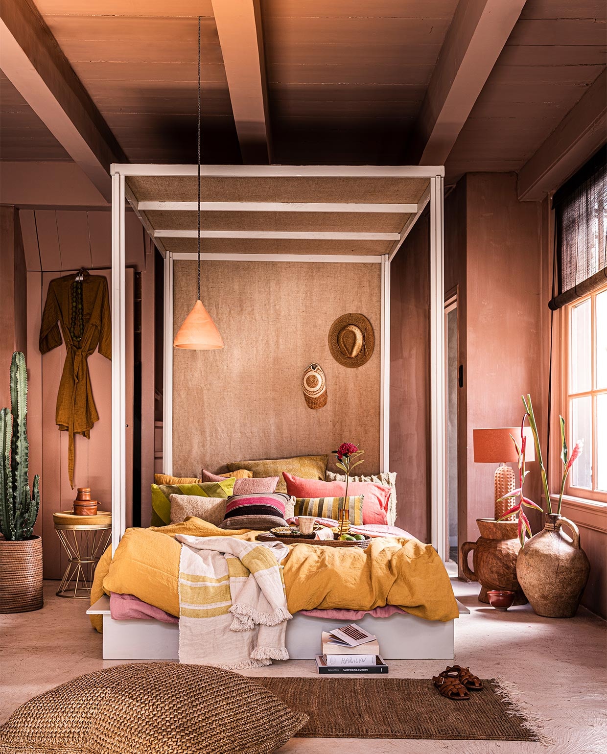 Verfkleur op wand Cypria van Carte Colori, 2,5 liter € 136,80, plafondlamp Maron, prijs op aanvraag, goudkleurige wand metallic stuc via Estudio, prijs op aanvraag, raambekleding Indivipro, prijs op aanvraag, bord Wonki Ware € 23,-, mok Wonki Ware € 19,- (brechtmurreatelier.nl). Handgemaakt hemelbed, prijs op aanvraag (com-anders.nl). Roze kussen met bruine streep € 125,-, roze kussen links daarboven € 163,- geel en roze linnen kussens, onderdeel van dekbed, per stuk € 39,-, geel en roze linnen dekbed­overtrekken, per stuk € 325,-, langwerpig lichtgeel kussen € 215,-, dienblad, onderdeel van bijzettafel € 275,-, pet € 59,-, vaas € 1260,-, mand waar cactus in zit, onderdeel van salontafel € 275,-, kralenketting € 119,-, plaid met gele streep € 115,-, vloerkleed, 150×78 cm € 245,-, poef, 80×60 cm € 495,-, kussen met streepmotief achteraan € 249,- (couleurlocale.eu). Bruine glazen vaas Balloon van Normann Copenhagen, 19×7 cm (hxØ) € 36,80, rood schaaltje Merci van Serax, 15 cm € 21,40, groen langwerpig gestreept kussen van HKliving € 32,95, linnen servet van HKliving, set van 2 € 15,45, geel/groen kussen € 34,95 (vtwonen.nl). Bloem in vaas en cactus, prijs op aanvraag (plantje.nl). Geel kussen met stiksels, 70×70 cm € 147,50, ochtendjas € 85,- (archive-store.nl). Hoed € 34,99 (koconceptstore.nl). Staande lamp € 119,- (sissy-boy.com). Houten kruk vanaf € 339,- (polspotten.nl). Hanglamp voor bed € 29,-, groene schaal € 16,- (householdhardware.nl). Sandalen € 59,99, set leren doosjes op tafeltje, vanaf € 29,99 (zarahome.com). Goudkleurig tafeltje € 169,-, onderste boek op stapel € 37,50 (maisonnl.com). Bovenste boek op stapel € 40,- (sukha.nl). Overige boeken privébezit. vtwonen 07-2021 | styling Liza Wassenaar | fotografie Sjoerd Eickmans