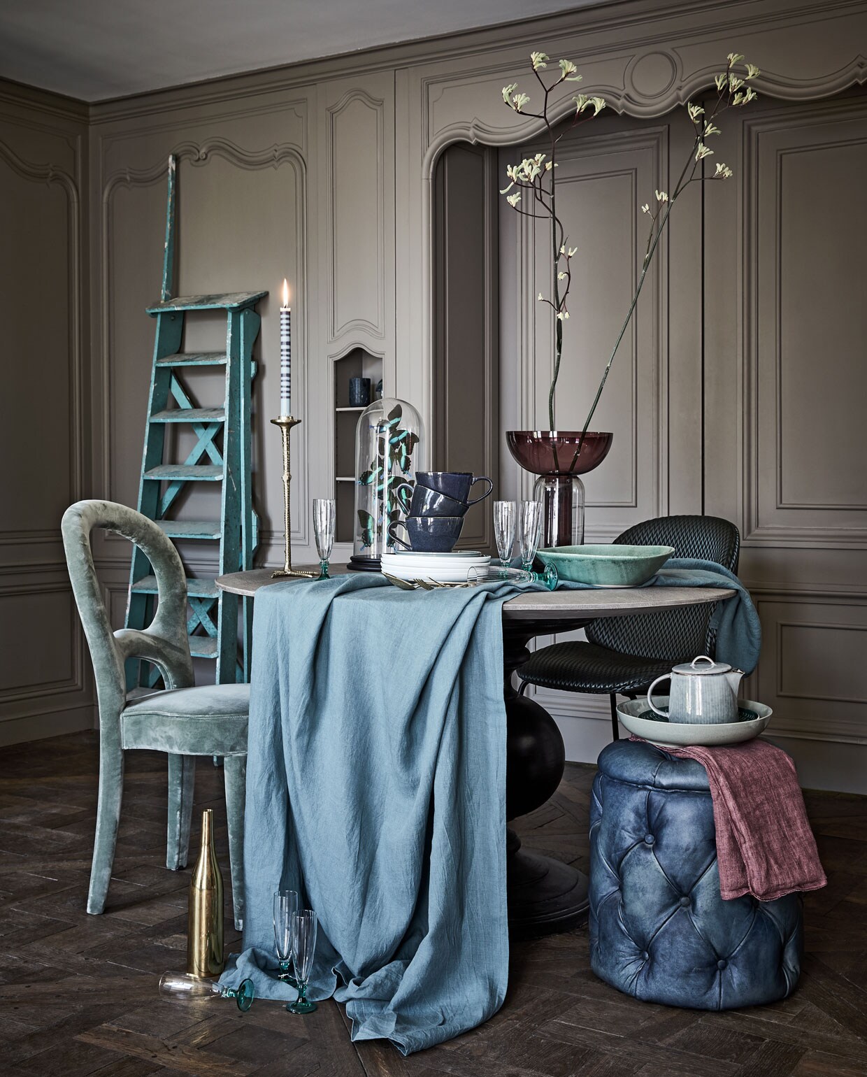 Tafel rond met zwarte poot Ø 130 cm, poef blauw (www.purefurniture.com). Stoel groen Promemoria (covanderhorst.nl). Stoel midden, gouden fles (edha-interieur.nl). Ladder (burbri.nl). Hoge vaas (homestede.nl). Kaars, theepot (maisonnl.com). Borden It’s my match van Villeroy &amp; Boch, marmeren mok van Zuiver (vtwonen.nl). Bestek goud vanaf (zarahome.com). Kandelaar, linnen tafelkleed, blauwe mokken (loods5.nl). Lichtblauwe schaal (hm.com). Glazen op groene voet (wildschut-antiques.com). Paars linnen (bungalow.dk). Stolp met kunstvlinder (weldaad.com). Groene schaal privébezit. vtwonen 10-2019 | styling Liza Wassenaar | fotografie Alexander van Berge
