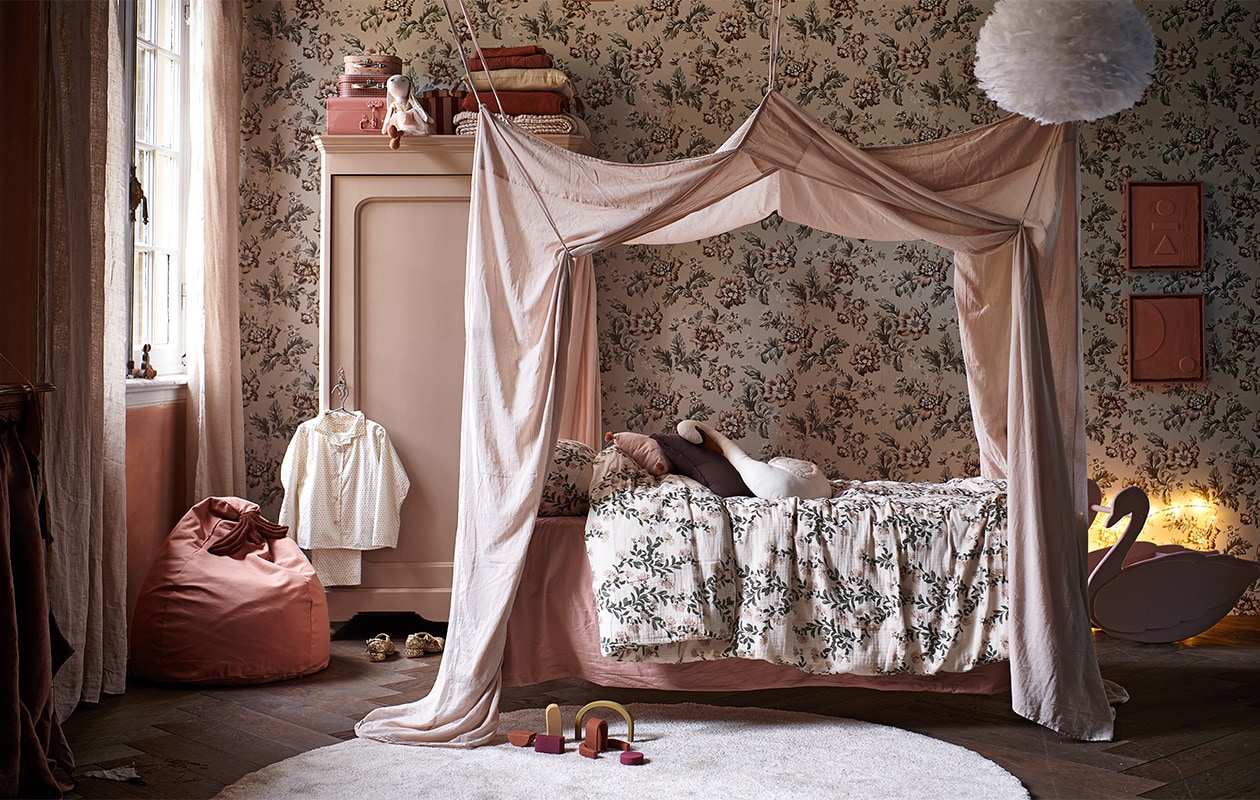 Behang Rosenholm Wheat van Sandberg € 111,56 (sandbergwallpaper.com). Wit spijlenbed € 135,- (burbri.nl). Oude houten kast € 125,- (vandijkenko.nl). Juten vloerkleed Dots van Ferm Living € 39,- (vtwonen.nl). Dekbedovertrek Honeysuckle Muslin van Garbo &amp; Friends, 140×200 cm € 90,- (lidor.nl). Kussen in vorm van huis Celia Mink van Camomile London € 39,95, gevlochten opbergmand appelvorm van Ferm Living € 45,-, miniatuur-items van Maileg: roze, houten bed € 35,-, keuken € 70,-, badkamerwastafel € 32,50, ballet dance room met big sister mouse € 57,50 (storeofdaydreams.com). Mini-schommel € 9,95 (feloufamilyhouses.nl). Roze ronde poppenhuistafel € 12,95 (maileg.com). Zwart poppenhuis € 12,95 (ilovespeelgoed.nl). Knuffel konijn € 22,99, houten poppenhuismeubels bed, kast en stoel € 19,99 (zarahome.com). Wanddecoratie ballon Byon Dusty small € 29,95 (psikhouvanjou.nl). Stof voor gordijnen roze gewassen linnen € 39,95 (kniphal.nl). Vloer visgraat eiken bruin geolied uit de vtwonen collectie € 69,95/m2 (karwei.nl). vtwonen 13-2021 kids special | styling Kim van Rossenberg | fotografie Sjoerd Eickmans | Assistentie Sanne van der Beek, Judie Jonker, Kim Suos