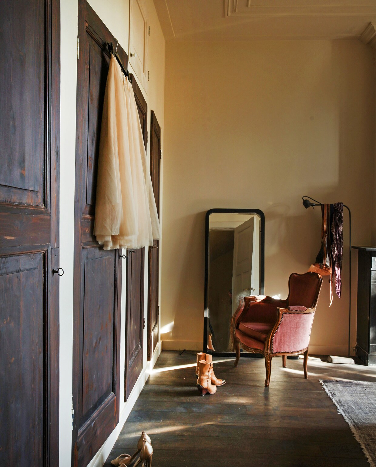 Achter het behang in de slaapkamers op de verdieping zaten blinde deuren verstopt. Nieuw opgeschuurd werden het de deuren van opbergkasten. Vintage spiegel, vloerkleed en fauteuil. Vloerlamp Brecht Murré Atelier. vtwonen 09-2021 | Styling Liza Wassenaar | Fotografie Irisdorine