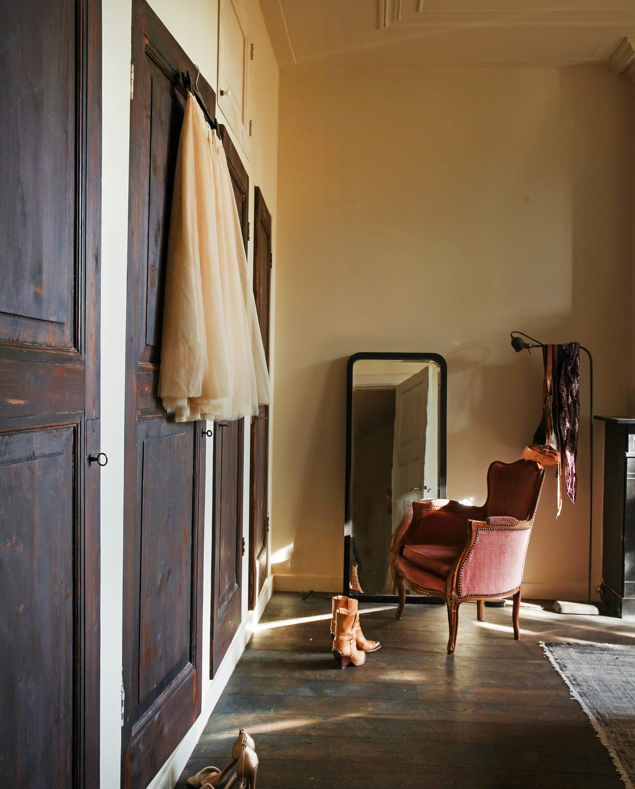 Achter het behang in de slaapkamers op de verdieping zaten blinde deuren verstopt. Nieuw opgeschuurd werden het de deuren van opbergkasten. Vintage spiegel, vloerkleed en fauteuil. Vloerlamp Brecht Murré Atelier. vtwonen 09-2021 | Styling Liza Wassenaar | Fotografie Irisdorine