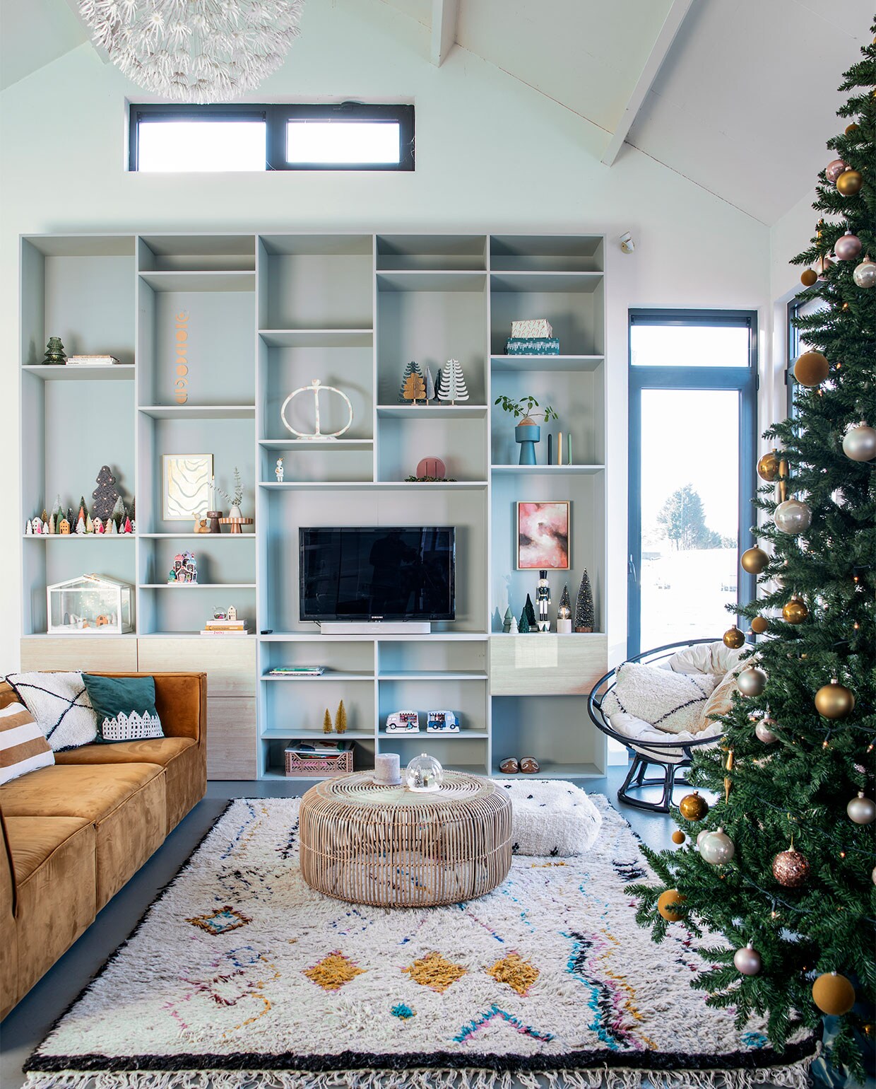 Wandkast op maat gemaakt. Winterhuisje Lemax. Kerststal in kas en hanglamp van Ikea. Papieren huisjes Jurianne Matter. Boompjes Ferm Living. Ronde/ovale witte kandelaar Junoon. Schilderij met wolken van Wendy Lammerschaag. Houten notenkraker Jysk. Mini-kerstbomen Hema en Jysk. Groene vaas, gestreept kussen Oyoy Living Design. Bank Sofacompany. Kleed, poef en wit kussen Living Maroc. Salontafel HKliving. Stoel Casa. Groen kussen V. at the City. Overig herkomst onbekend. vtwonen 12-2021 | productie Insidehomepage | styling Laura Gommans | fotografie Louis Lemaire