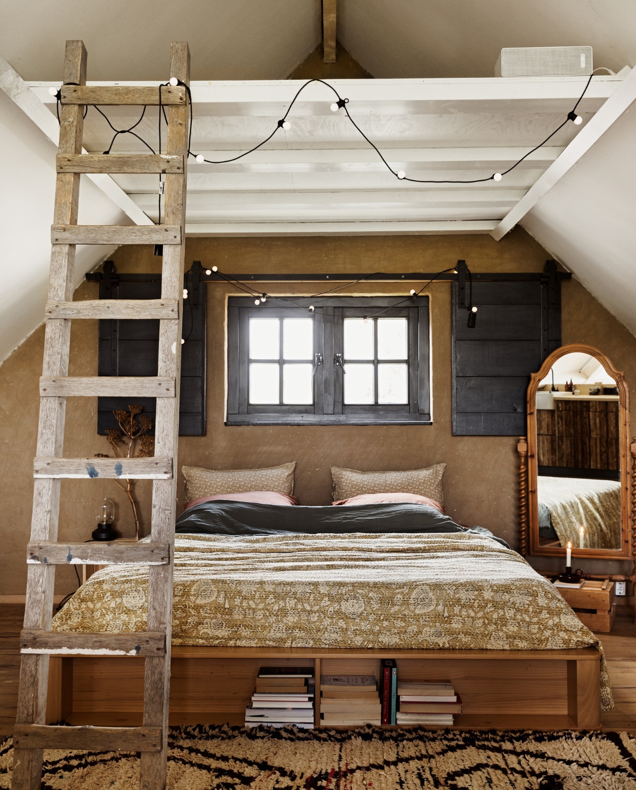 Bed Made. Ladder en spiegel Marktplaats. Sprei Indiase Khanta doek via Etsy. Kussensloop Zara Home. Lichtsnoeren Ikea. Vloerkleed The Souks. Muur afgewerkt met leemstuc. Overig onbekend. vtwonen 13-2022 | styling Ilona Jongepier | fotografie Dana van Leeuwen