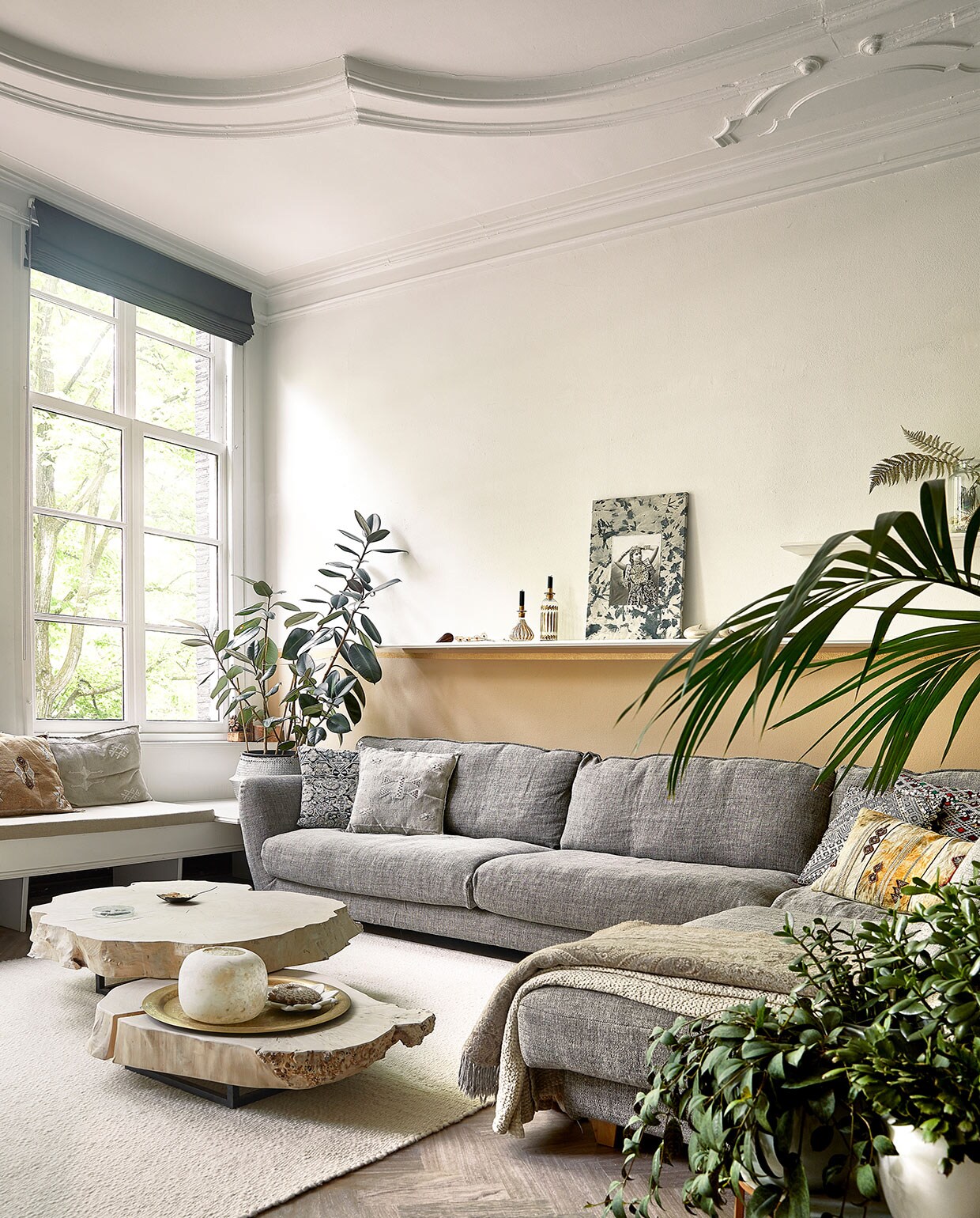 Raambekleding en vloer zaten al in het huis. Bank in vensterbank op maat gemaakt. Loungebank Seats. Kussens, plantenmand, tafels, plaid, kaarsenhouders/vazen, marmeren schaaltje en dienblad Zenza. Wollen vloerkleed Helsinki van Vloerkleden-winkel. Muurverf zelf gemengd. Bijzettafels Heerenhuis Manufactuur, fossiel van schelp, koperen schaaltje MaisonNL. Portret door dochter Naomi gezeefdrukt en geborduurd. vtwonen 06-2021 | productie Coco Features | styling Linda van der Ham | fotografie Peggy Janssen