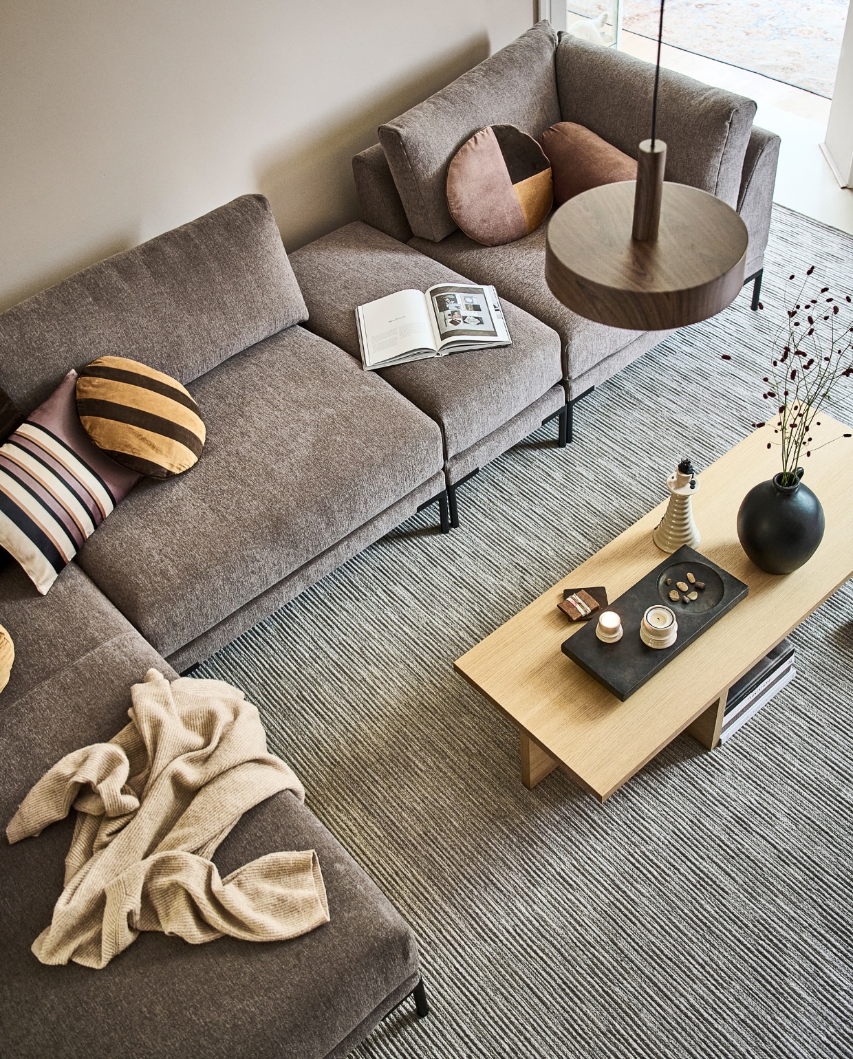 Vloer marmoleum in kleur Mergel per m2 € 50,40 (pag. 107). Vloerkleed Ridge vanaf € 149,- (pag. 103). Elementenbank Couple in stof nr. 12 in deze opstelling€ 3946,- (pag. 44), Kussens vanaf € 29,95 (pag. 57) Salontafel Angle € 519,- (pag. 48). Vaas zwart € 69,95 (pag. 58). Kandelaar zandkleurig vanaf € 29,95 (pag. 62). Waxinelichthouder zandkleurig (set van 2) vanaf € 29,90 (pag. 62). Hanglamp Woody vanaf € 79,99 (pag. 78). JA | vtwonen catalogus 2022-10 | styling Kim van Rossenberg  | fotografie Sjoerd Eickmans