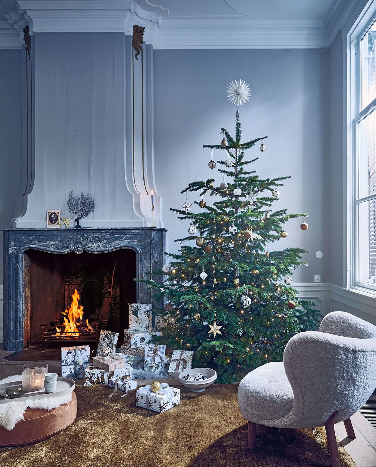 Nordmann kerstboom (janvanvulpenboomkwekerij.nl). Kerstlampjes diamantverlichting warm wit van Lumineo, 29,9 m, vloerkleed Nami van Bolia, 170×240 cm, suède poef Time van Bloomingville, dienblad van Serax 53×31,5 cm, schapenvacht van Weltevree, espressomokken Grid van Broste Copenhagen 0,15 l (vtwonen.nl). Fauteuil bekleed met schapenvacht van &amp;Tradition, 81x83x75 cm (bxdxh) (homestede.nl). Glazen windlicht, papier-maché schaal, transparante glazen ballen, ballen met veertjes (nordal.eu). Handbeschilderde ballen met strepen en stippen (fermliving.com). Spiegelsterren, eikels en diamantvormige glazen ornamenten (sissy-boy.com). Gouden vallende sterren, gouden vredesduif, guirlande met gouden blaadjes, stervormige piek, gedecoreerde dozen set van 3 (bungalow.dk). Okergele fluwelen kerstballen set van 2, wit-goud-marmer pakpapier, pakpapier met sterren, pakpapier met zwart-wit bos, satijnlint (hm.com). Overig privébezit. vtwonen 12-2019 | styling Cleo Scheulderman | fotografie Jeroen van der Spek