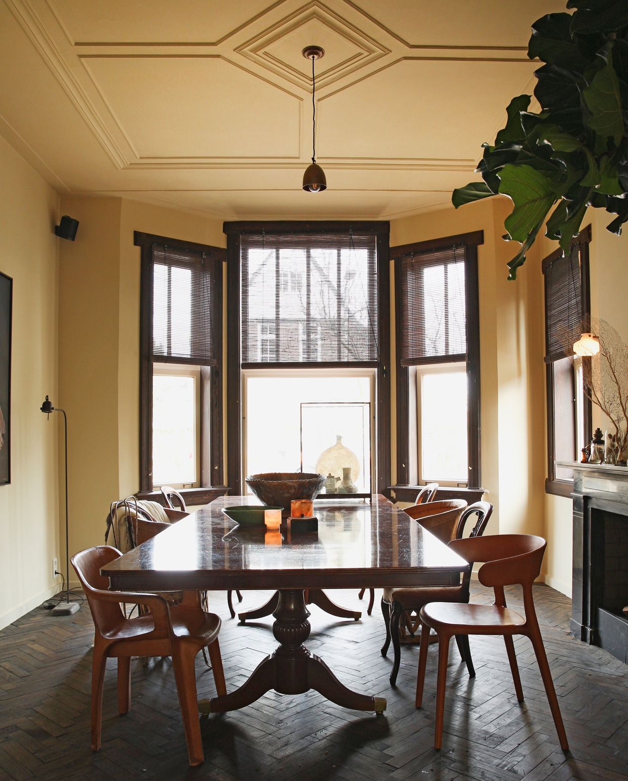 Vloer en kozijnen bruin gelakt. Antieke tafel. Met leer overtrokken plastic tuinstoel en vloerlamp van Brecht Murré Atelier. Overige stoelen kringloop en Marktplaats. De verlichting boven tafel is een tijdelijke oplossing: ‘We zoeken nog een kroonluchter of monumentale hanglamp.’ Verf muur en plafond F3.09.75 van Histor. Schalen Brecht Murré Atelier, Mobilia en Household Hardware. vtwonen 09-2021 | styling Liza Wassenaar | fotografie Irisdorine