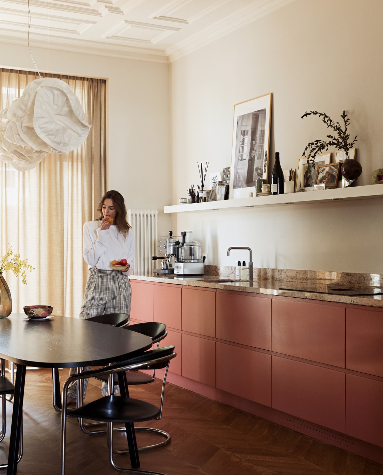 Rechte keuken zonder keukenkastjes, Houten vloer gelegd in Hongaarse punt laminaatenparket.nl. Stoelen en gordijnen Marktplaats. Eettafel Studio Henk. Hanglamp Belux Cloud van Frank Gehry. Keuken basis van Ikea, fronten Frontz. Granieten aanrechtblad De Keukenbladen Fabriek. Kookplaat Bora. Kraan Quooker. Keukenmachine Magimix. Koffiezetapparaat Isomac. Geurstokjes Marie-Stella-Maris. Cocktailshaker erfstuk van Lidians grootouders. Servies van Louks grootouders. Madeleinevorm en Droste chocoladevorm antiekmarkt. Verfkleur achterwand Ral 9001. Verf plafond Ral 9010. Overig onbekend. NEE | vtwonen BK8- 5 2022 | styling Ilona Jongepier |  fotografie Dana van Leeuwen | tekst Jana Voyvodich