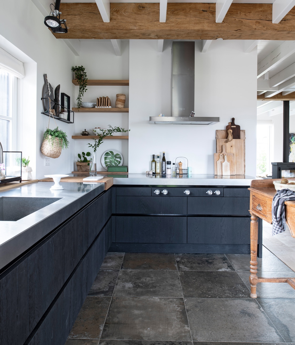 Keuken met rvs-werkblad Buro Logge, taartplateau kringloop, hangplantLoods 5, houten planken aan de muur en houten snijgedeelte Böhmer Project.Bord met blad Action, afzuigkap Smeg, houten snijplanken Dutchdeluxes enKitchen Trend. Muurrek Woood met daarin een Afrikaans beeldje gekocht opeen markt in Kenia, fotolijst Atelier Sukha. Houten bakjes, ronde plank enkleine snijplanken HKliving. vtwonen 13-2020 | Productie Insidehomepage | Styling Marlies Does | Fotografie Louis Lemaire | Tekst Cathelijne van Wingerden \n\nLandelijke keuken