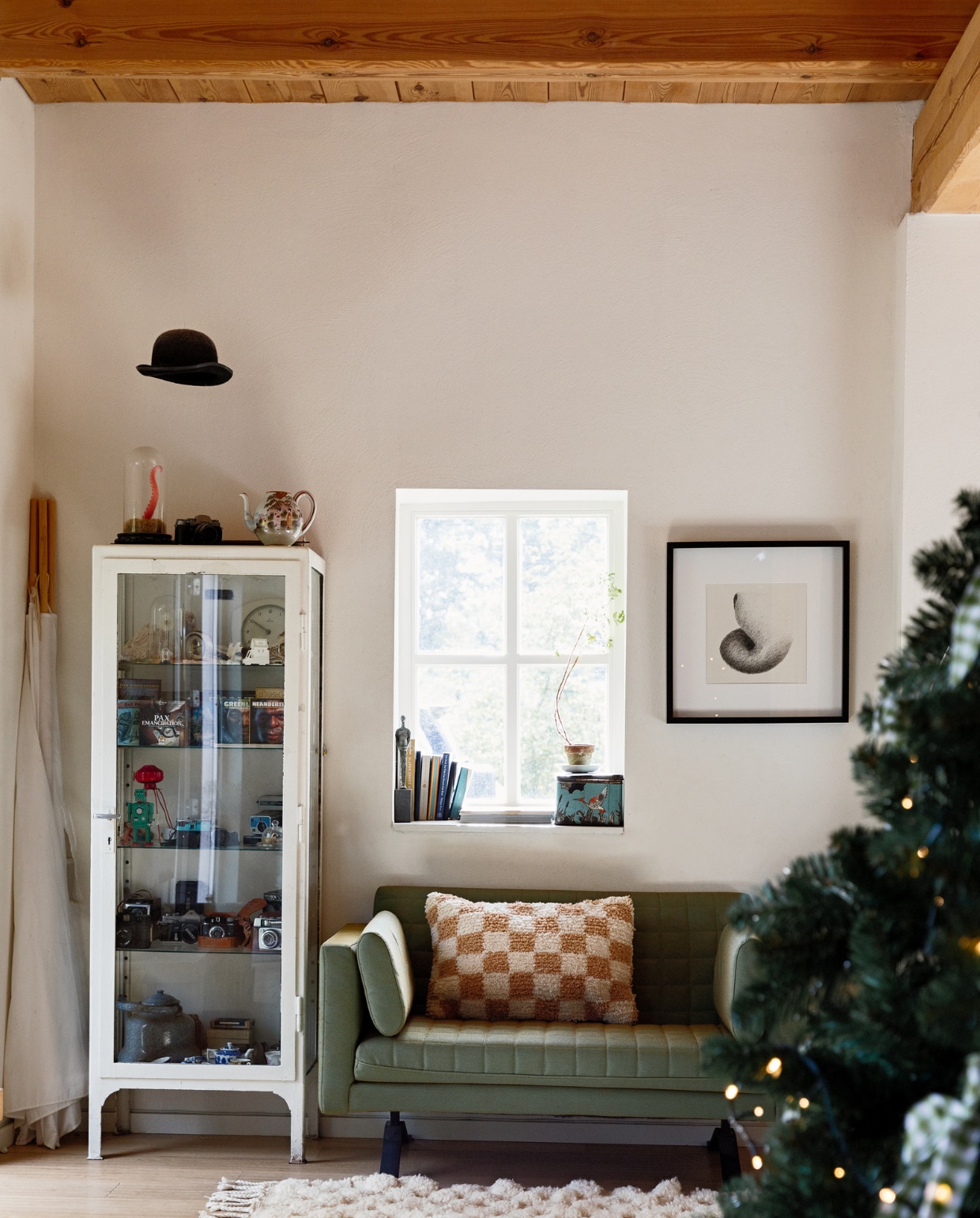 Bank Kilian van Pilau. Medicijnkast vintage. Kussen en vloerkleed The Souks. Kunstwerk gemaakt door Eva’s vader, lijst Ikea. Hoed van Eva’s opa. In de kast: verzamelingen. vtwonen 13-2022 | styling Ilona Jongepier | fotografie Dana van Leeuwen