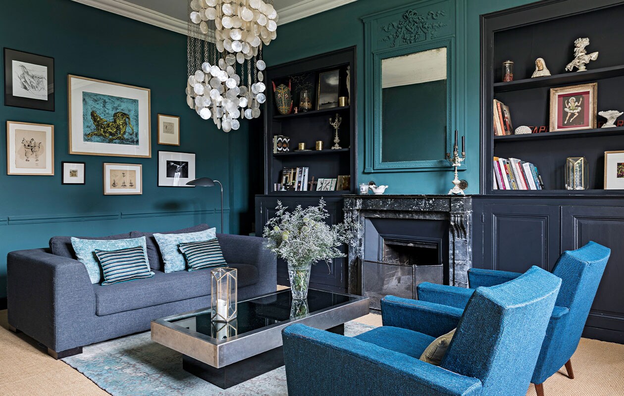 Bank van Maisons du Monde, fluwelen en zijden kussens Le Monde Sauvage, vintage salontafel van Willy Rizzo, parelmoer kroonluchter van Verner Panton, karpet gevonden in Amsterdam. Blauwe fauteuils van een rommelmarkt in Bellême. Blauwe muurverf Emery &amp; Cie, donkere muurverf Farrow &amp; Ball. NEE | vtwonen 4-2022 |  styling  Marie-Maud Levron | fotografie Yann Deret | tekst Anne-Catherine Scoffoni | tekstbewerking Chris Muyres