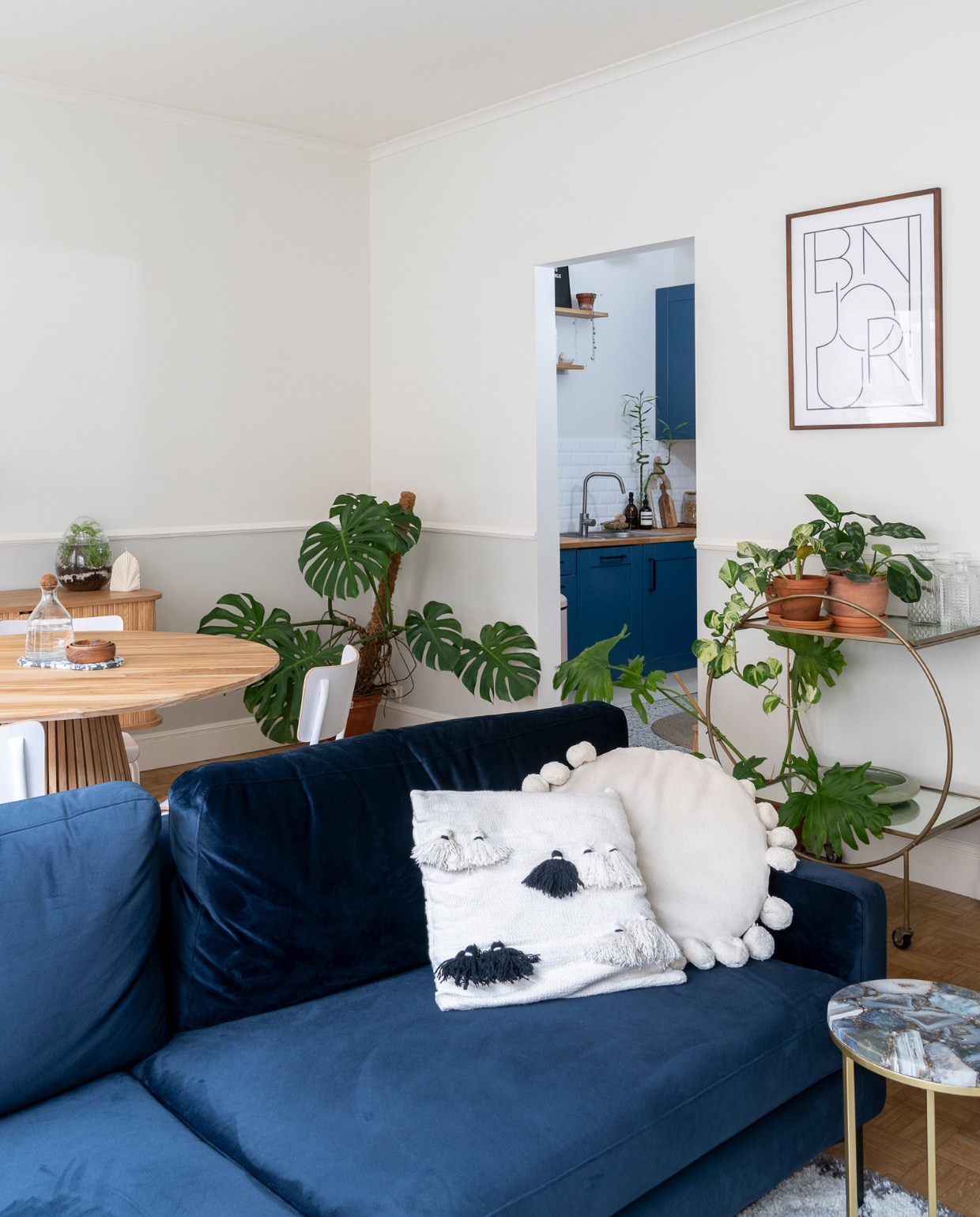 Muren geschilderd in Lovely White WE Z042 en Newspaper Grey WE Z090 van Boss Paints via Colora. Ronde tafel Fonq, blauwe bank Sofa Company, kussens La Redoute, H&amp;M Home en meegenomen uit Bali. Bijzettafel en rek op wielen Sissy-Boy. Lijst Bonjour van H&amp;M Home. Verlichting Westwing. vtwonen 09-2022 | Fotografie Jonah Samyn | Tekst Katrien Depoorter