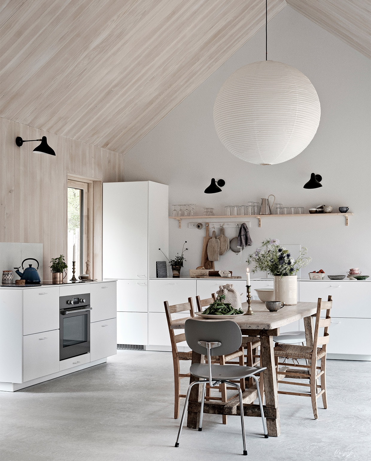 Keuken, wandrekken, glazen en hoge krijtwitte vaas Ikea. Eettafel en snijplanken Andrea Brugi. Metalen stoel Egon Eiermann, houten stoelen vintage. Vergelijkbare plafondlamp Lampion. Wandlampen Serge Mouille. Theeketel Le Creuset. Zilveren kan uit Griekenland, groen bord uit Marokko. Theedoek Aiayu. Overig onbekend. NEE | vtwonen binnenkijken special 03-2022 | productie Revolver, Living Inside | fotografie Mikkel Tjellesen | styling Marie Monrad Grounbøl