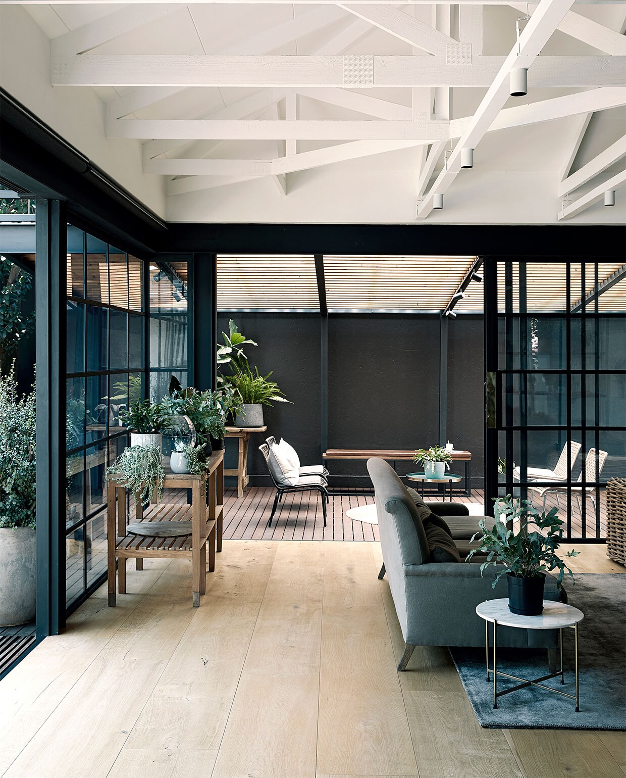 Bank Mezzanine Interiors. Rieten bank Weylandts. Bank rechts en stalen stellingkast Live Simple. Tapijt en ronde bijzettafel Hertex. Plantentafel en bloempotten kringloopwinkel. Overig onbekend. NEE | vtwonen binnenkijken special 2021 | productie Bureaux | styling Sven Alberding | fotografie Elsa Young