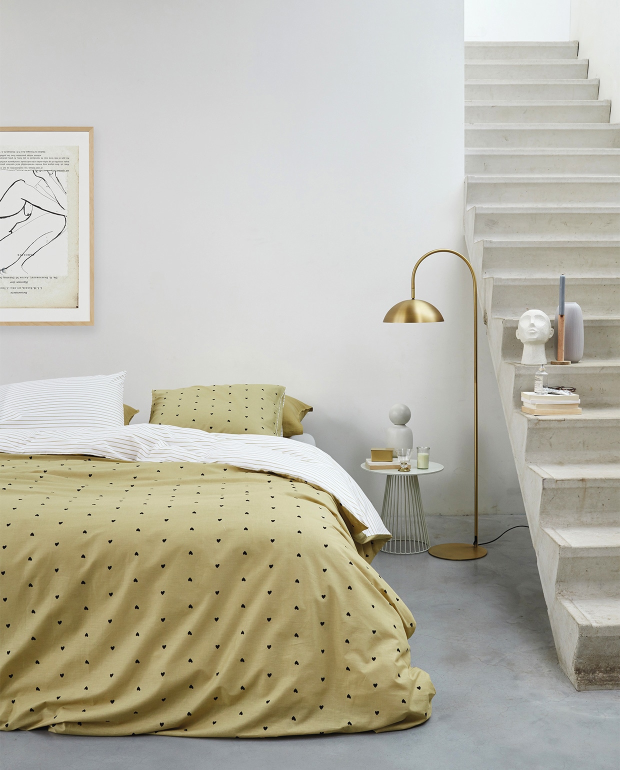 Katoen perkal dekbedovertrek Striped Hearts in kleur geel, 140×200/220 cm € 59,95, 200×200/220 cm € 109,95 en 240×200/220 cm € 119,95 (inclusief kussenslopen). Ook verkrijgbaar in wit met zwarte hartjes en strepen.M.m.v. vtwonen.nl (lamp van vtwonen), letoile.store (poster in lijst, messing bakje), loods5.nl/design (bijzettafel, vaas met boldeksel), loods5.nl (glas, kaars in glas, wit object hoofd, houten kandelaar). Overig privébezit. JA | vtwonen huiscollectie 04-2021 | styling Danielle Verheul | fotografie Richard Smit | productie Tanja Saarberg