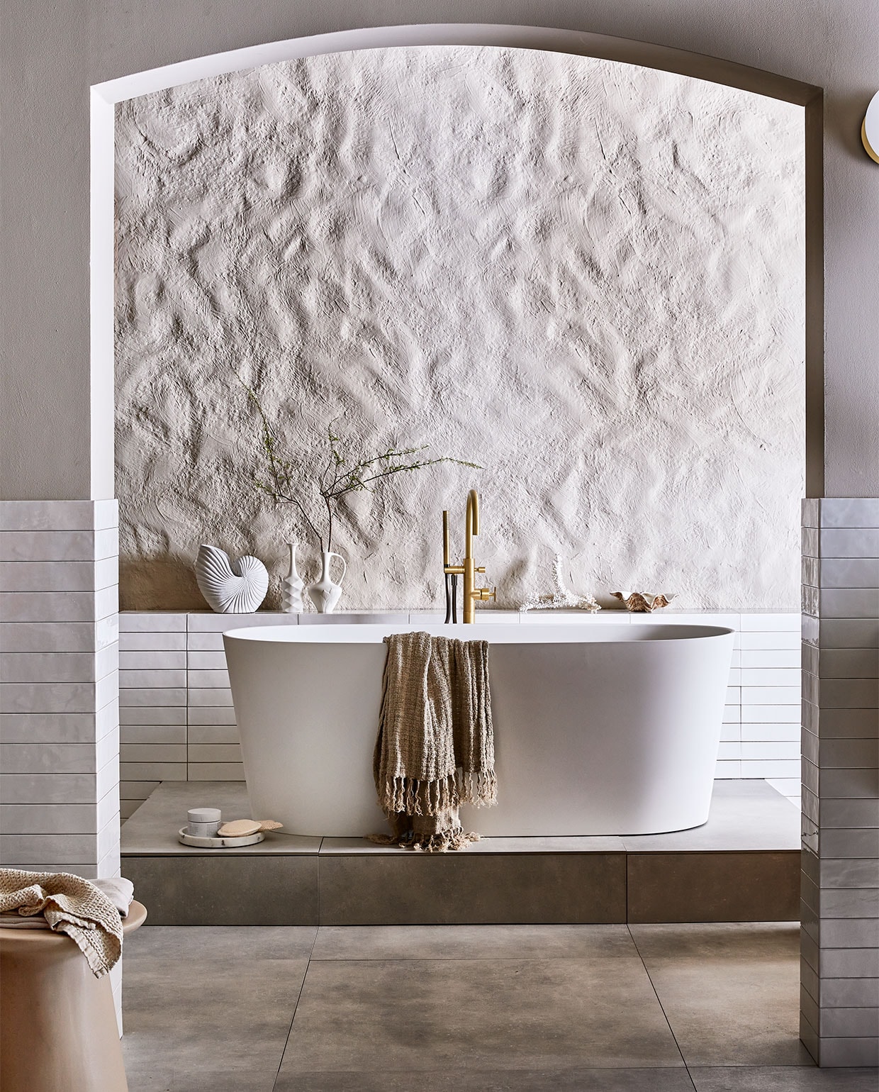 Vloertegel Mold XL Cement, 90×90 cm. Wandtegel achter wastafel Marrakesh, kleur Nieve, glans, 6,5×40 cm (lxb). Wastafel Tank, beton, kleur Concrete, 10x120x46 cm (hxbxd). Onderbouwkast Cube, eikenhoutfineer, kleur Oak, 30x120x43,5 cm (hxbxd). Wandkraan Flame, kleur Bronze, inbouwdeel. Bad Tub. Badmengkraan Flame, kleur Bronze, vrijstaand M.m.v. vtwonen.nl (muurverf kleur Flax, spiegel Ferm Living, wafelhanddoek Marc O’Polo), hkliving.nl (kruk, kleine witte vazen), nordal.eu (grote schelp, schelpvormige vaas, linnen badlakens, marmeren zeepdispenser), weldaad.com (marmeren schaaltje), hm.com (loper, grote marmeren schaal op vloer). De achterwand kreeg stuc effectief in kleur Flax van vtwonen (gemaakt door setbouw Milo Kol). JA | vtwonen 08-2021 | styling Cleo Scheulderman | fotografie Jeroen van der Spek