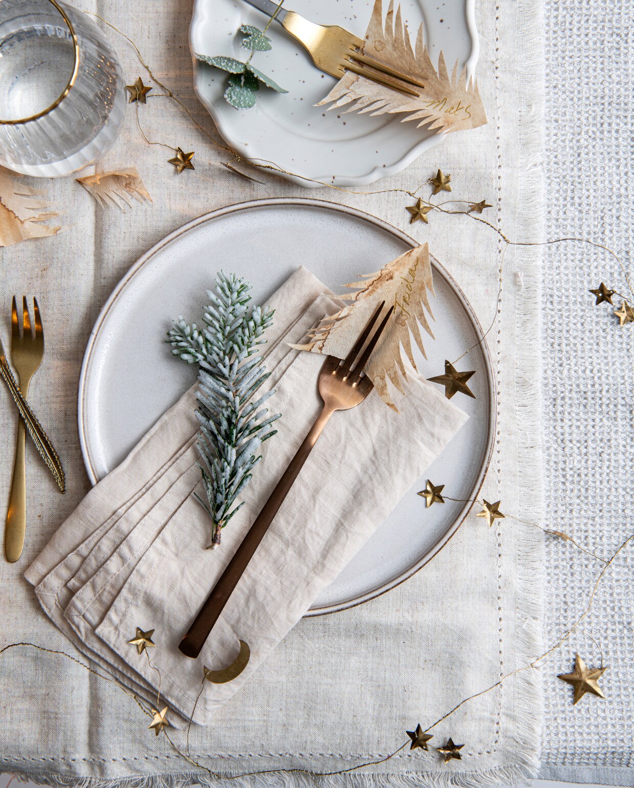 Glas met goudkleurige rand, soortgelijk vanaf € 5,99, porseleinen bord met bruine spikkels € 5,99, wit keramieken bord € 9,99, katoenen mousseline servetten, set van 2 € 7,99 (hm.com). Rvs bestekset van Gusta, 16-delig € 48,49 (vtwonen.nl). Wafeltheedoek van katoen en linnen € 15,- (arket.com). Brass kerstslinger met manen en sterren € 14,95 (sissy-boy.com). vtwonen special Kerst Couture 12-2022 | styling Janneke Peters | fotografie Louis Lemaire