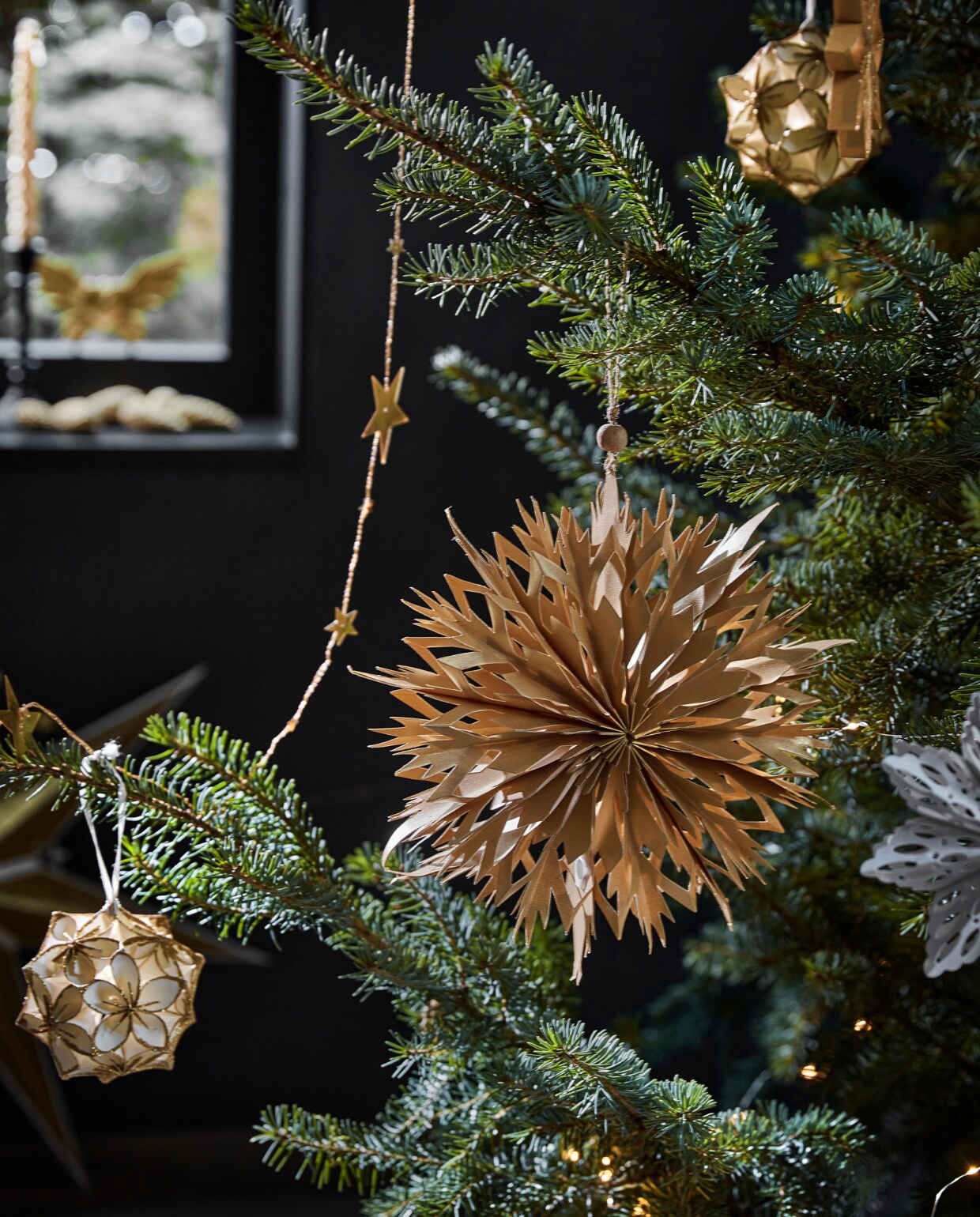 Goudkleurige metalen slinger met sterren, 210 cm (l), wit papieren ornament bloem met glitter, 10 cm (Ø) (ook verkrijgbaar in zwart met zilver). Goudkleurig papieren ornament, 20x5,5 cm (Øxd), goudkleurig ornament ster, 15x1,5 cm (Øxd). vtwonen 12-2022 | productie Tanja Saarberg, Isa Hoevens | styling Kim van Rossenberg | fotografie Peggy Janssen