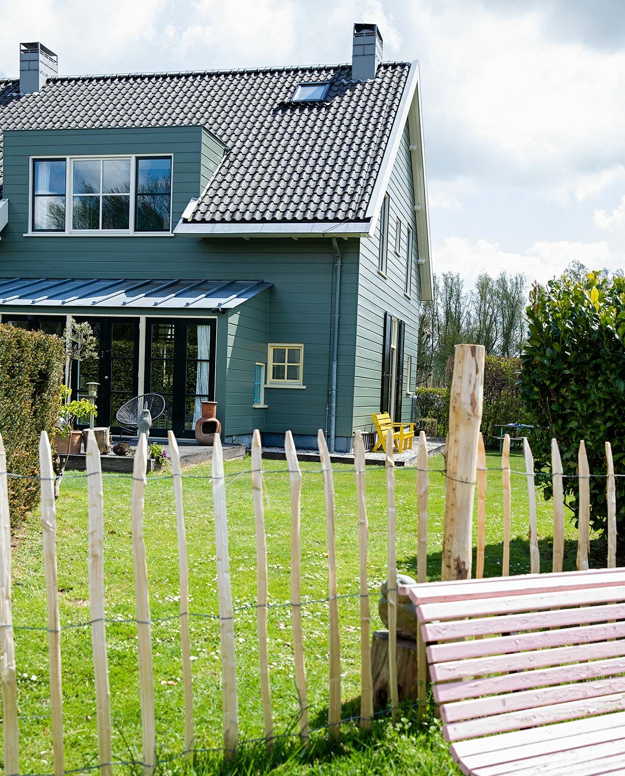 Het huis is aan de buitenkant afgetimmerd met hout, maar heeft een betonnen constructie. De kleur is bepaald door de monumentencommissie en mag niet worden veranderd. Tuinbank van de kringloop geschilderd in Nancy’s Blushes van Farrow &amp; Ball. vtwonen 07-2021 | styling Ilona Jongepier | fotografie Dana van Leeuwen