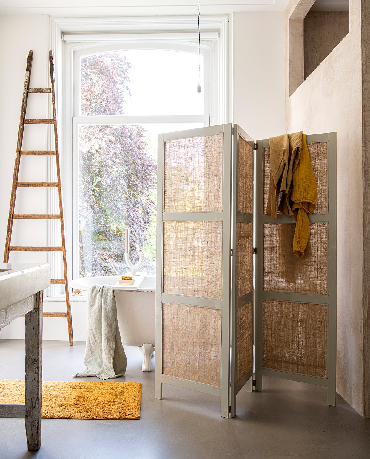 Jute kamerscherm DIY uit vtwonen special 05-2022. Katoenen badmat, 60×100 cm € 49,95, groene linnen wafelhanddoek € 39,95 (yumeko.nl). Houten zeepschaal Hinoki € 18,-, badborstel van Iris Hantverk € 30,- (thefinestore.com). Kandelaar van Urban Nature Culture € 39,95 (zaanschfaamwebshop.nl). Zeep van Kusala € 7,95, okergele linnen top € 50,- (atelierhop.com). Jurk Nina in kleur Sunflower Yellow € 85,- (lidor.nl). Overig privébezit. vtwonen special DIY 05-2022 | styling Myla Griese | fotografie Louis Lemaire