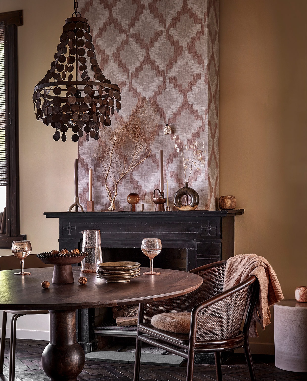 Behang Grounded Tribal 220603 van BN Walls, 100×53 cm € 37,95 (behangwereld.nl). IJzeren kroonluchter Balou, 29x29x55 cm (bxdxh) € 319,00 (hoffz.nl). Kandelaar met drie poten Brazilian Nights € 24,95, keramieken object vlinder € 10,95 (alagonda.nl). Roze natuurstenen kandelaar € 16,67, natuurstenen kandelaar blok € 15,15, donkerbruine eetkamerstoel, teakhout en rattan, 58×77 cm (bxh) € 814,40 (nordal.com). Gestreepte dinerkaars € 2,25, bruine kandelaar met hengsel € 6,95, glazen dop van karaf € 34,95 (vita32.nl). Houten kandelaar voor stompaars € 10,95, taupekleurige dinerkaars € 2,25, cirkelvaas € 33,95, roze windlicht € 59,95, gebreid vest € 59,99 (loftloft.nl). Minikandelaar € 6,50, minikaars € 0,45, bruin windlicht € 17,50, rond kussen € 16,50 (stijldepot73.nl). Droogbloemen (@tuinvanjudith). Beige eetkamerstoel Oda van Broste Copenhagen, 76x40x52 cm (hxbxd) € 577,25 (vtwonen.nl). Eetkamertafel Blanco van BePureHome, mango- en walnoothout, 120×75 cm (Øxh) € 629,- (basiclabel.nl). Roze wijnglazen per stuk € 11,50, roze karaf € 21,75 (bungalow.dk). Bruine schaal op poot € 80,- (@studio.cherrymoon). Handgemaakte borden per stuk € 7,50 (@flowerchild.arnhem). Bijzettafel van Serax 32x32x29 cm (bxdxh) € 345,- (loods5.nl). Gebogen dinerkaars, object koraal en leren boeken in vensterbank privébezit. vtwonen 10-2022 | styling Demelza Krens | fotografie Peggy Janssen