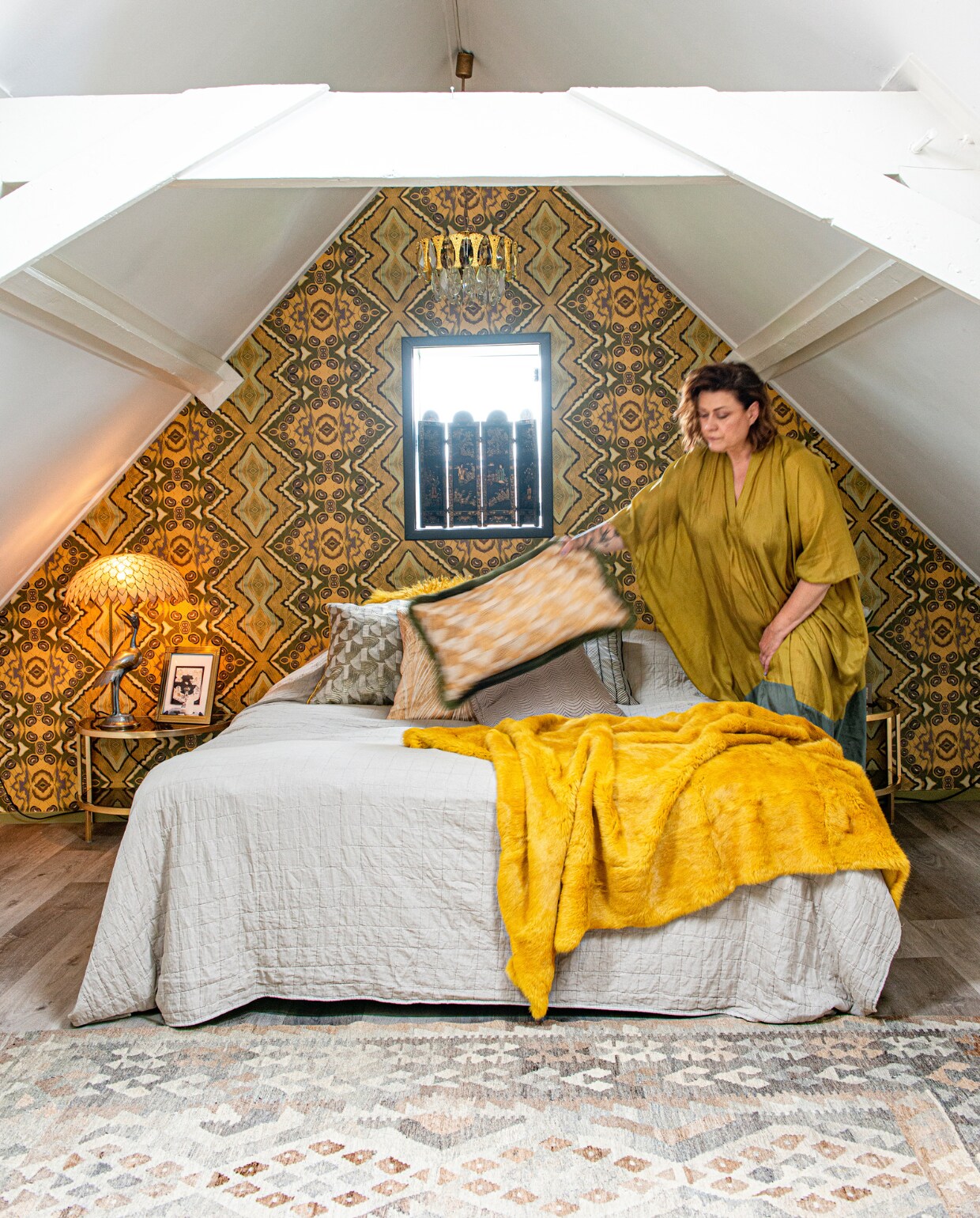 In het raam een mini-roomdivider uit een rommelwinkel, reiger tafellamp uit de jaren 60, half ovale nachttafels met getint glas en massief messing van onbekende fabrikant, fotolijst uit Duitsland, lamp van Gaetano Sciolari, kelim uit Afghanistan, behang Artwallcollection by Hanneke van de Pol, kussens Mippies, grijze sprei Jysk, gele sprei van lamsvacht herkomst onbekend. NEE | vtwonen 11-2022 | Productie @debinnenkijkers | Styling Jeske Weel | Fotografie Caroline Coehorst | Tekst Chris Muyres