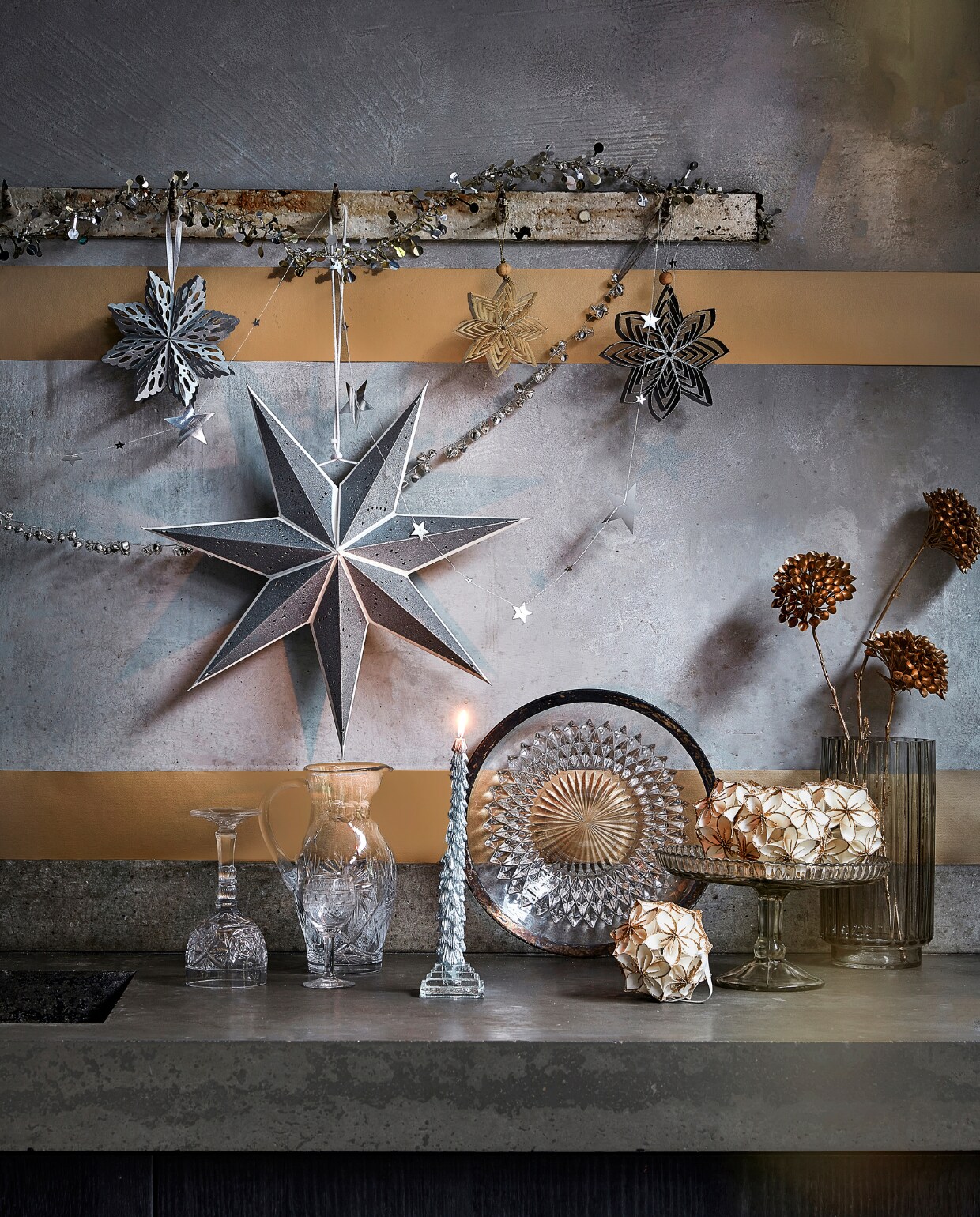 Zilverkleurige slinger met ijzeren belletjes, 120 cm (l) € 7,99, zilverkleurige metalen slinger met sterren, 210 cm (l) € 3,49, zilverkleurig papieren ornament, 15×1,5 (Øxd) € 2,99, zilverkleurige papieren ster, 70×19 cm (Øxd) € 6,99, goudkleurig ornament van gerecycled papier, 15,5×3 cm (Øxd) € 2,69, zwart ornament van gerecycled papier, 15,5×3 cm (Øxd) € 2,69, zilverkleurige kaars met glitter, per 2 € 6,99, wit papieren ornament bloem met glitter, 10 cm (Ø) € 5,99 (ook verkrijgbaar in zwart met zilver). vtwonen 12-2022 | productie Tanja Saarberg, Isa Hoevens | styling Kim van Rossenberg | fotografie Peggy Janssen