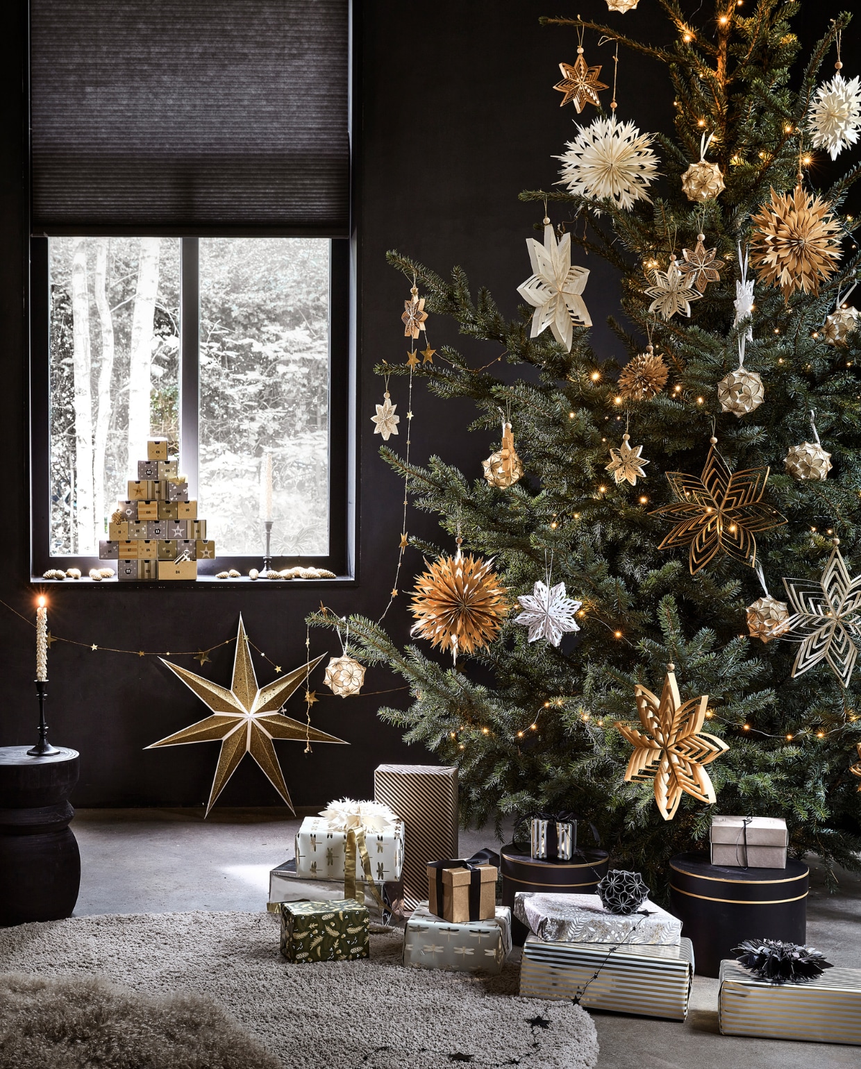 Kartonnen adventskalender € 27,99, goudkleurige kaars met glitter, per 2 € 6,99, goudkleurige papieren ster, 70×19 cm (Øxd) € 9,99, goudkleurige metalen slinger met sterren, 210 cm (l) € 3,49 (ook verkrijgbaar in zilver). In de boom: diverse papieren ornamenten in de kleuren goud, wit, zilver en zwart, per stuk vanaf € 2,49, zilverkleurige lichtslinger warm wit met 30 ledlampjes op batterijen inclusief display en timer, 300 cm (l) € 3,99. vtwonen 12-2022 | productie Tanja Saarberg, Isa Hoevens | styling Kim van Rossenberg | fotografie Peggy Janssen
