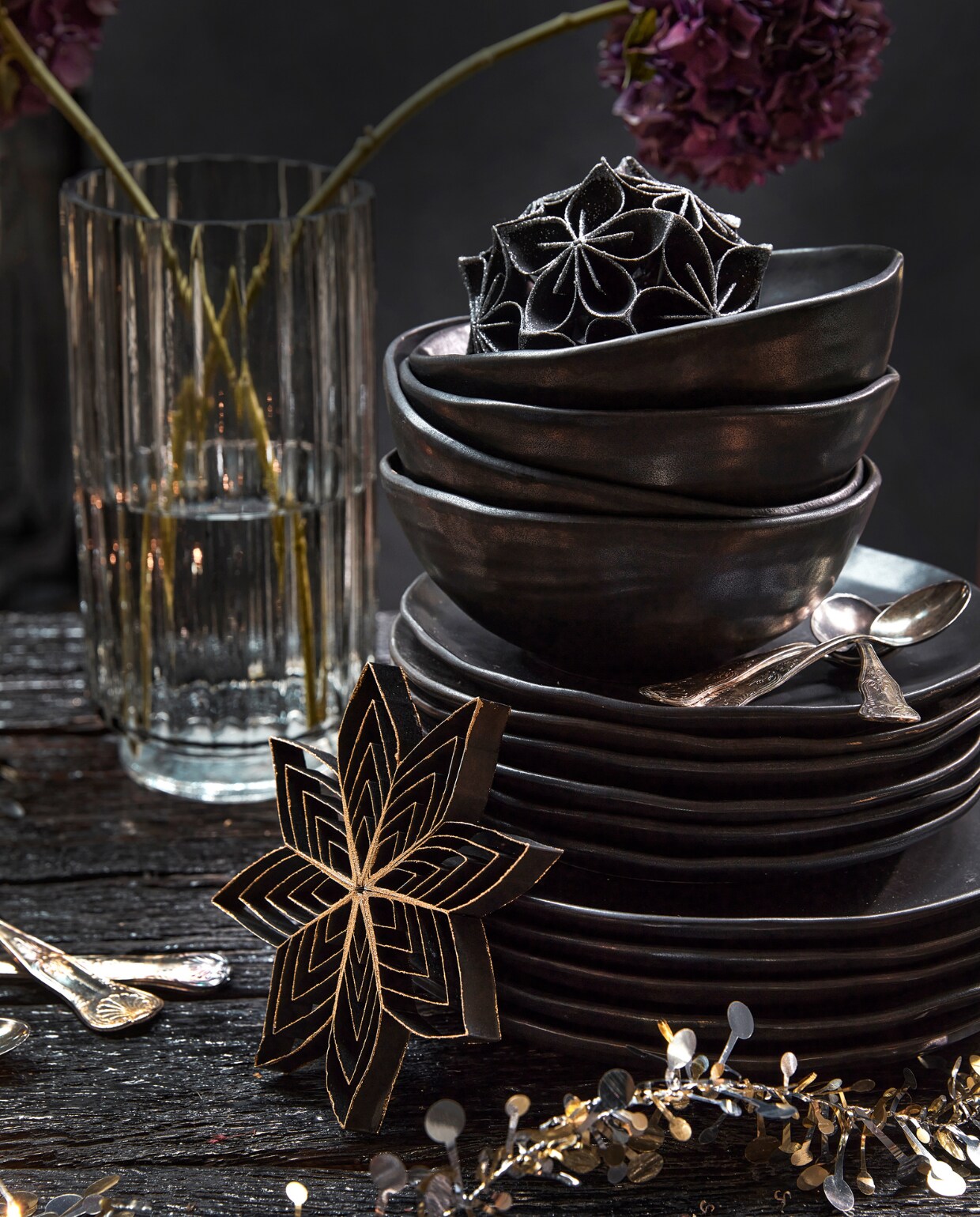 Zwart papieren ornament bloem met glitter, 10 cm (Ø) € 5,99, zwarte papieren ster van gerecycled papier, 15,5×3 cm (Øxh) € 2,69, goud- en zilverkleurige slinger met sterren en bolletjes van kunststof, 120 cm (l) € 7,99. vtwonen 12-2022 | productie Tanja Saarberg, Isa Hoevens | styling Kim van Rossenberg | fotografie Peggy Janssen