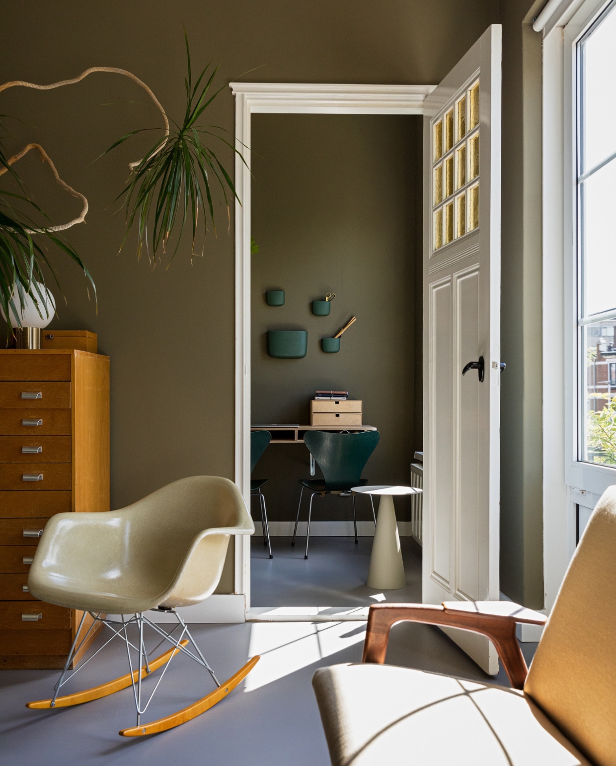 Muurkleur RAL 7002. Vintage plastic schommelstoel RAR van Eames voor Vitra. bank van Yngve Ekström voor Pastoe. Oude papierkast uit een school. Vlinderstoel van Fritz Hansen via Vintagemarket12. Bureau zelfgemaakt. Bijzettafel Karwei. Kistje en bollamp rommelmarkt. Wandbakjes Normann Copenhagen. Overig onbekend. vtwonen 10-2022 | styling Ilona Jongepier | fotografie Dana van Leeuwen | tekst Monique van der Pauw