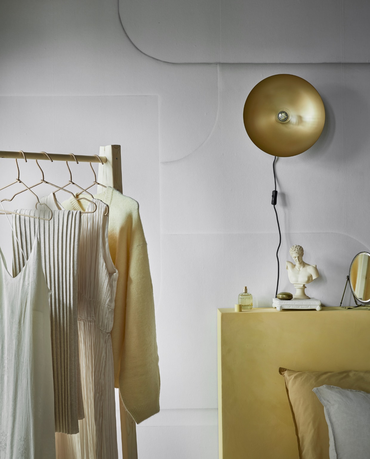 Fotobehang Soft 3D in Light Grey, 6 banen van 280×50 cm, totaal 280×300 cm (lxb) € 149,-, per m² € 17,74. Metalen wandlamp Disk in antiek brons exclusief lichtbron, 33×15 cm (Øxh) € 84,99. Kledingrek DIY-ontwerp, kijk voor de werkbeschrijving op vtwonen.nl/diy/ vtwonen 12-2022 | productie Tanja Saarberg | styling Sanne Ketelaar | fotografie Peggy Janssen