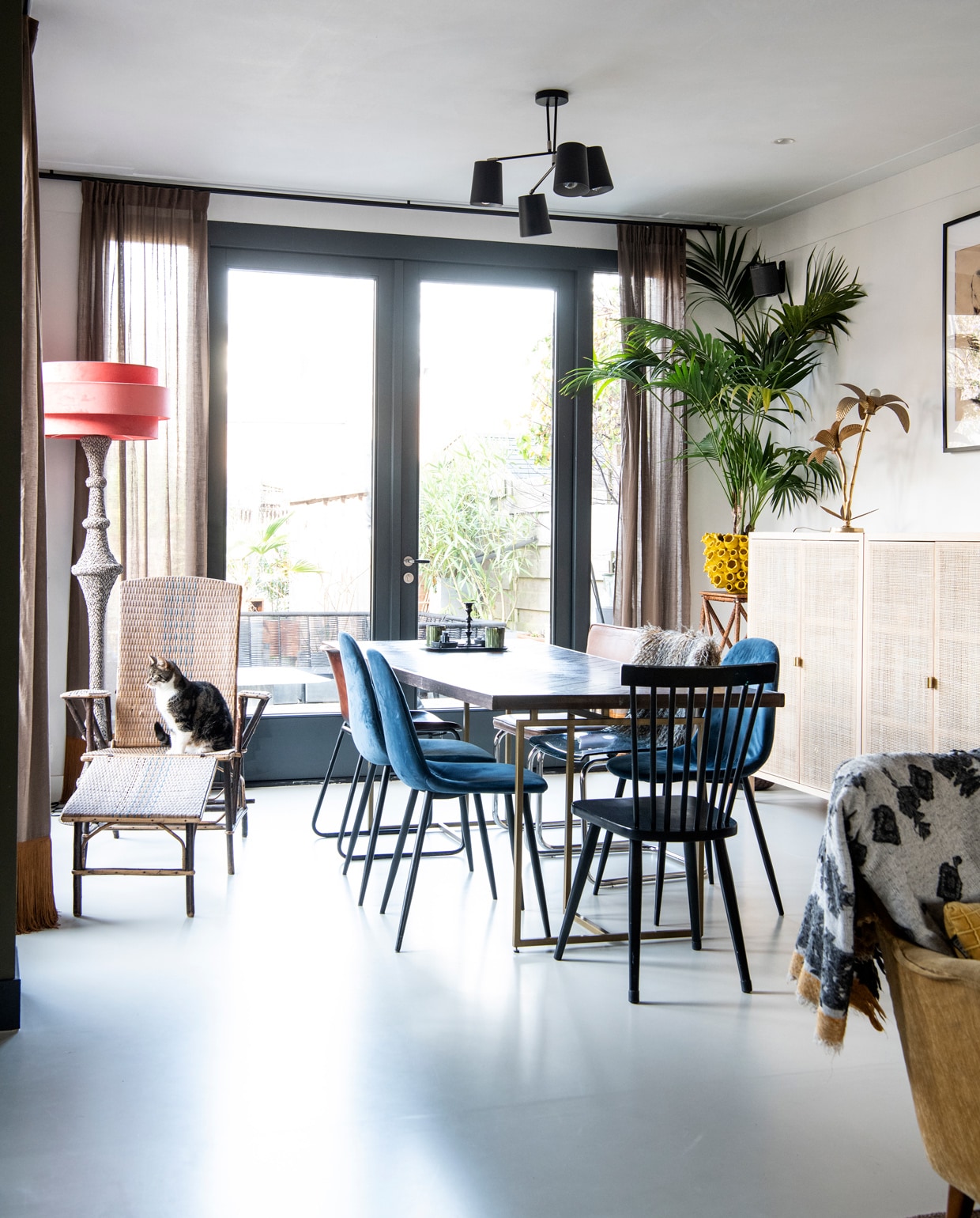 Vintage rotan loungestoel gekocht bij een garageverkoop. Lampvoet Loods 5, kap Madame Garage. Eettafel Dutch Bone. Blauwe stoelen Kwantum. Zwarte stoel vintage. Plafondlamp Rietveld Licht. Gele plantenpot Colmore Diga. Wandkastje met webbing Ikea. Overig onbekend. vtwonen 10-2021 | Productie Insidehomepage | Fotografie Louis Lemaire | Styling en tekst Inge van Lieshout | Tekstbewerking Renate Dahlmans
