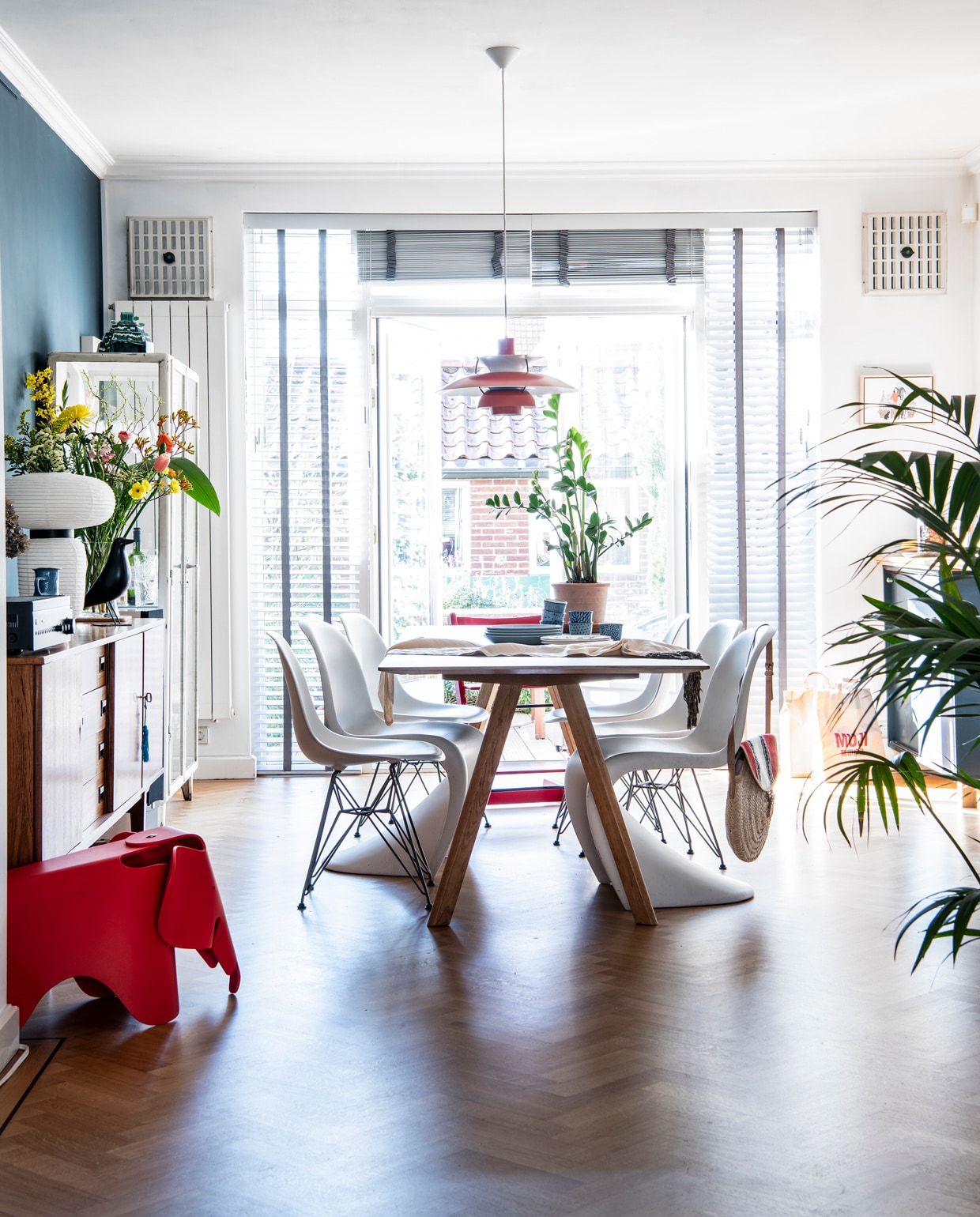 Muurverf links Ral 5008 van Engels Verf. De vloer lag al in het huis. Tafel CPH30 van Hay. Blauwe borden Iittala, witte borden met blauwe spetters Faye van Toogood, Japanse kopjes Shilla. Tas Dille &amp; Kamille. Panton-stoelen, Eames DSR-stoelen, Eames-olifantkruk en vogel House Bird van Vitra. Tripp Trapp-stoel Stokke. Vintage Lamp PH5 van Van Ons. Vintage kasten Loods 5. Witte lamp Formakami van &amp;Tradition. Plantenpot Arket, plant Sprinklr. vtwonen 13-2021 | Productie Insidehomepage | Styling Kim Timmerman | Fotografie Louis Lemaire | Tekst Inge van Lieshout | Tekstbewerking Mariska Keus