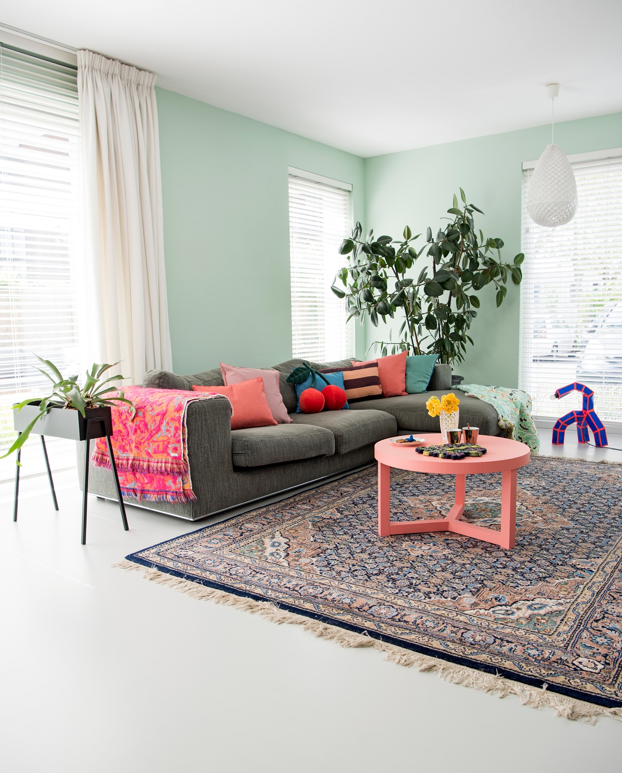 Bank Goossens. Gekleurde kussens Roos Soetekouw, kersenkussen merimeri.com, gestreept kussen HK Living. Roze Fringe plaid no. 1 en 5, Fun green Roos Soetekouw. Kleed marktplaats.nl. Plantenbak Kwantum. Witte lamp Studio Arntzen. Paper &amp; Tape lamp annebetphilips.com. Salontafel Zilverblauw voor Wown. Kopjes Pols Potten. Vaasje kringloop. Muurverf kleur Karma van Histor. vtwonen 12 binnenkijken special 2019 | styling Kim de Groot | fotografie Anke Leunissen