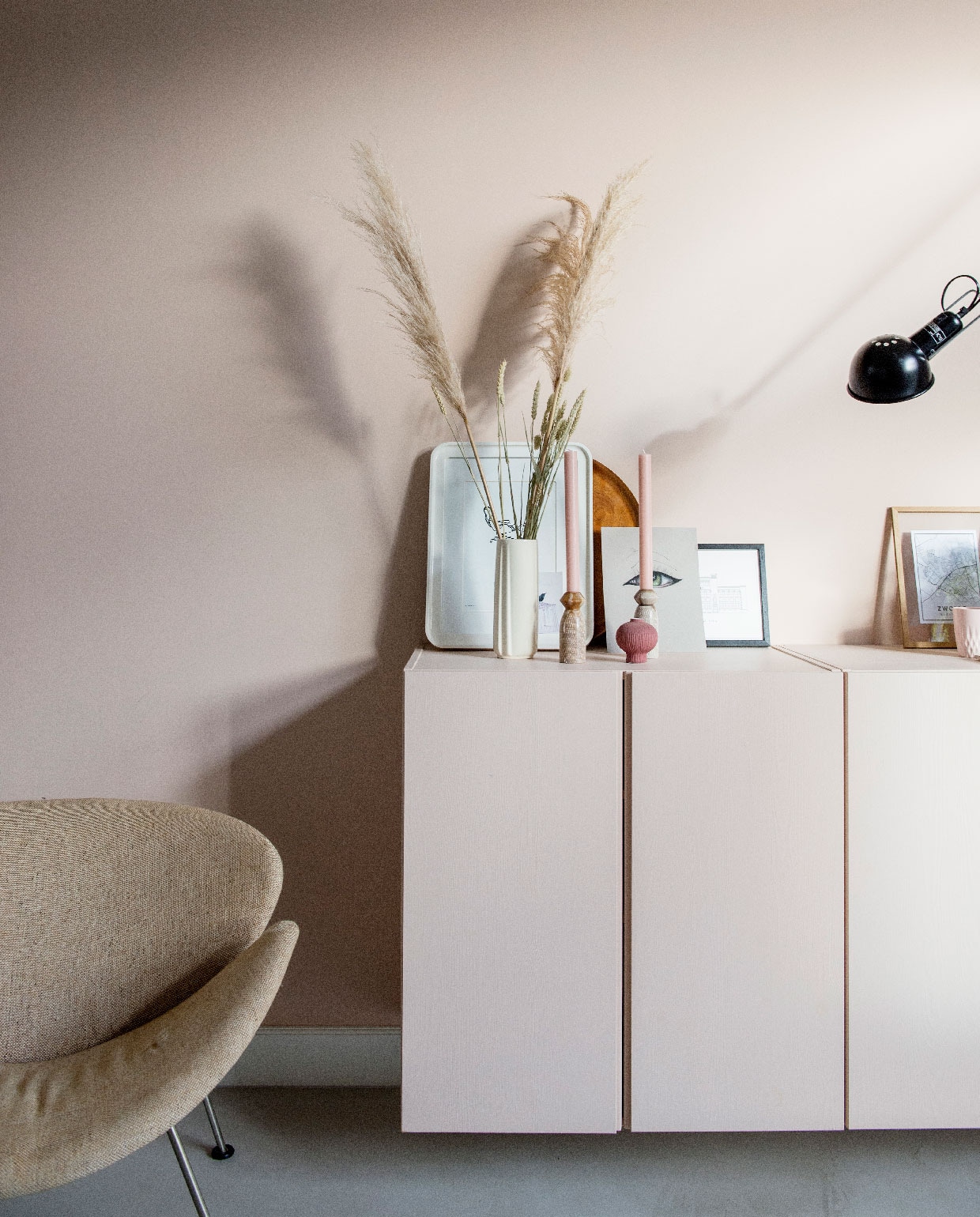 Muurverf Setting Plaster van Farrow &amp; Ball, vloer Leef-Beton gelegd door Het Nieuwe Stenen Tijdperk. Vintage stoel Orange Slice van Artifort Marktplaats. Ikea kastjes geschilderd in de kleur van de muur. Witte fotolijst Ikea, witte vaas en kaarsenhouders kringloop, kaarsen Winand Hazelaar. Print oog gemaakt door dochter Julia, zwarte fotolijst Desenio, houten fotolijst Moebe met daarin in een plattegrond van Zwolle. Wandlamp 265 Flos. vtwonen 06-2020 | binnenkijken in zwolle woonkamer met orange slice chair