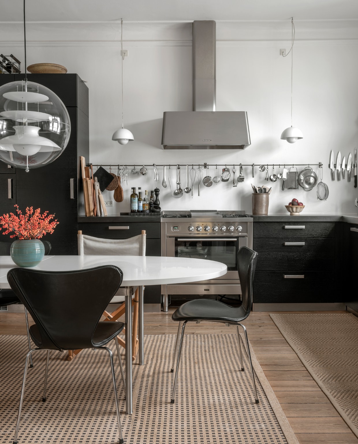 Tafel Marianne Wegner, twee Series 7 stoelen van Arne Jacobsen, vouwstoel Mogens Koch, hanglamp Globe boven de tafel en witte hanglampen Flowerpot boven aanrecht, alles Verner Panton. Fornuis en afzuigkap Ilve, ruim twintig jaar oud papiergaren vloerkleed van Woodnotes, stalen planken Ikea. Overig onbekend. vtwonen 11-2022 | productie Global Image | fotografie Peter Kragballen