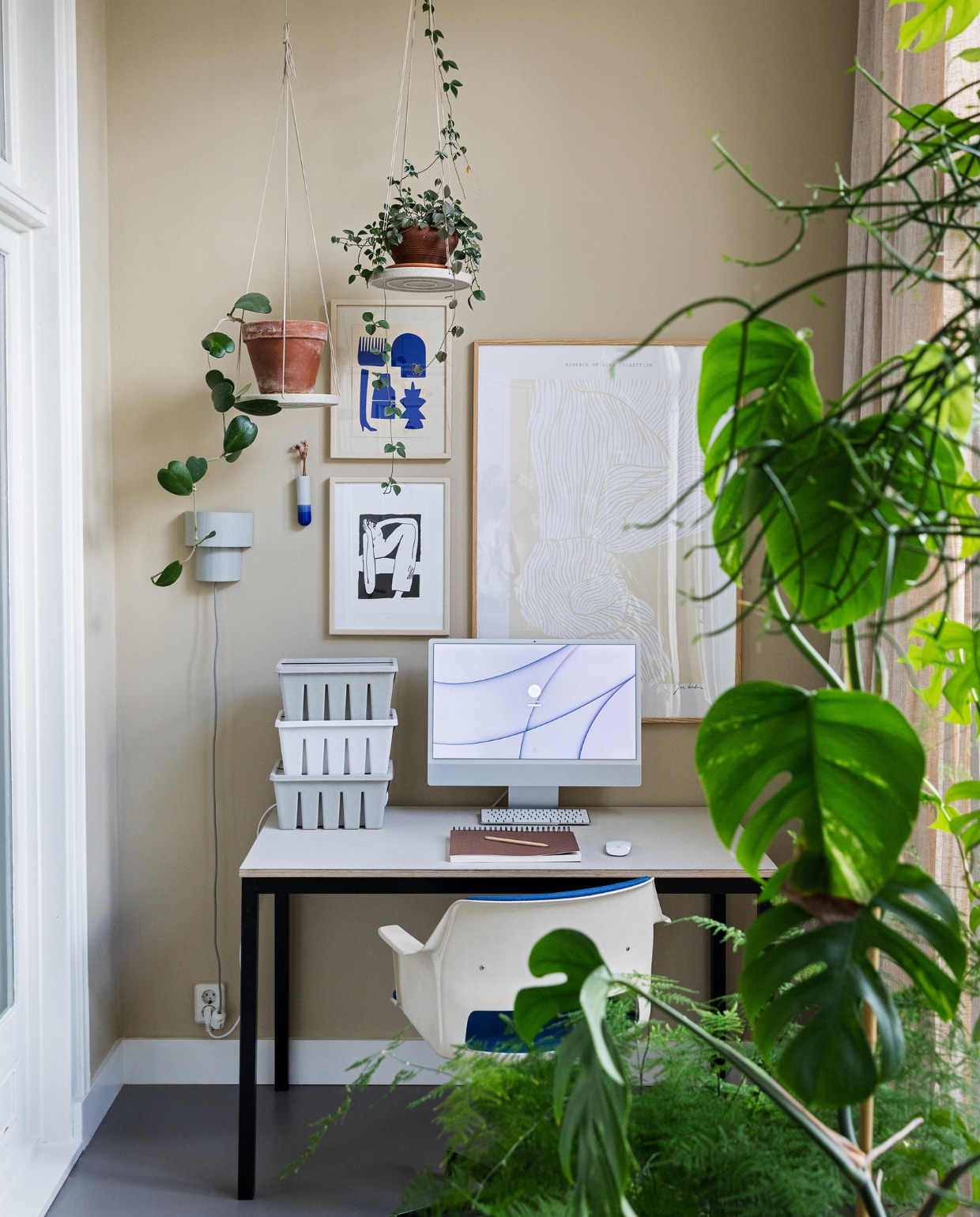 Muurkleur GN 080-08. Bureau zelfgemaakt van oud frame en linoneum blad. Bureaustoel Gispen. Print blauw van Silvia Visscher, print zwart-wit van Lucia Lenders, print beige, opbergdozen, wandvaasje van Harm en Elke, planten via Nørd Conceptstore. Wandlamp rommelmarkt. Plantenhangers Bloomingville. vtwonen 10-2022 | styling Ilona Jongepier | fotografie Dana van Leeuwen