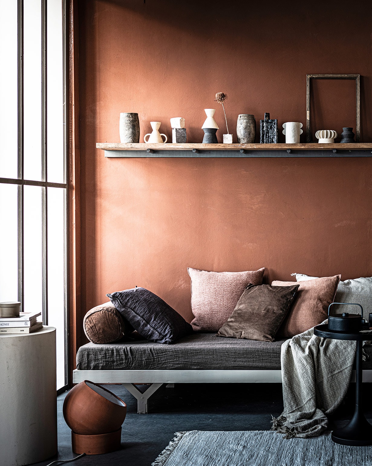 Muurkleur Fresco in Terracotta (pure-original.nl). Loungebed op maat gemaakt € 375,- (com-anders.nl). Op het loungebed: plaid Vice Versa in Terre van Maison de Vacances € 195,-, kussen Vice Versa Toile Nomade van Maison de Vacances € 146,-, kussen Vice Versa stone washed linnen van Maison de Vacances € 133,-, kussen off white Sabra Oblong XL € 113,- (couleurlocale.eu). Rond velvet kussen Bolster van Madam Stoltz € 39,25 (deens.nl). Bruin kussen van vtwonen collectie € 33,80, bruin velvet kussen € 30,95, plaid € 27,99, bijzettafel Jason van Zuiver € 99,95, lamp van klei van Serax € 124,95 (vtwonen.nl). Betonnen bijzettafel privébezit. Op de plank: hoge potten € 42,- (couleurlocale.eu), kleine vazen in wit, bruin en zwart uit de Earth series vanaf € 37,50, witte vaas met 4 oren Eyra € 50,- (studio-yen.com). Vaas abstracte vorm van Serax € 35,05, theepot Collage van Serax € 89,- (vtwonen.nl). Ronde zandkleurige doos € 19,- (fermliving.com). Vloerkleed € 19,99 (hm.com). Wandplank privébezit. vtwonen 03-2021 | styling Marlies Does | fotografie Sjoerd Eickmans